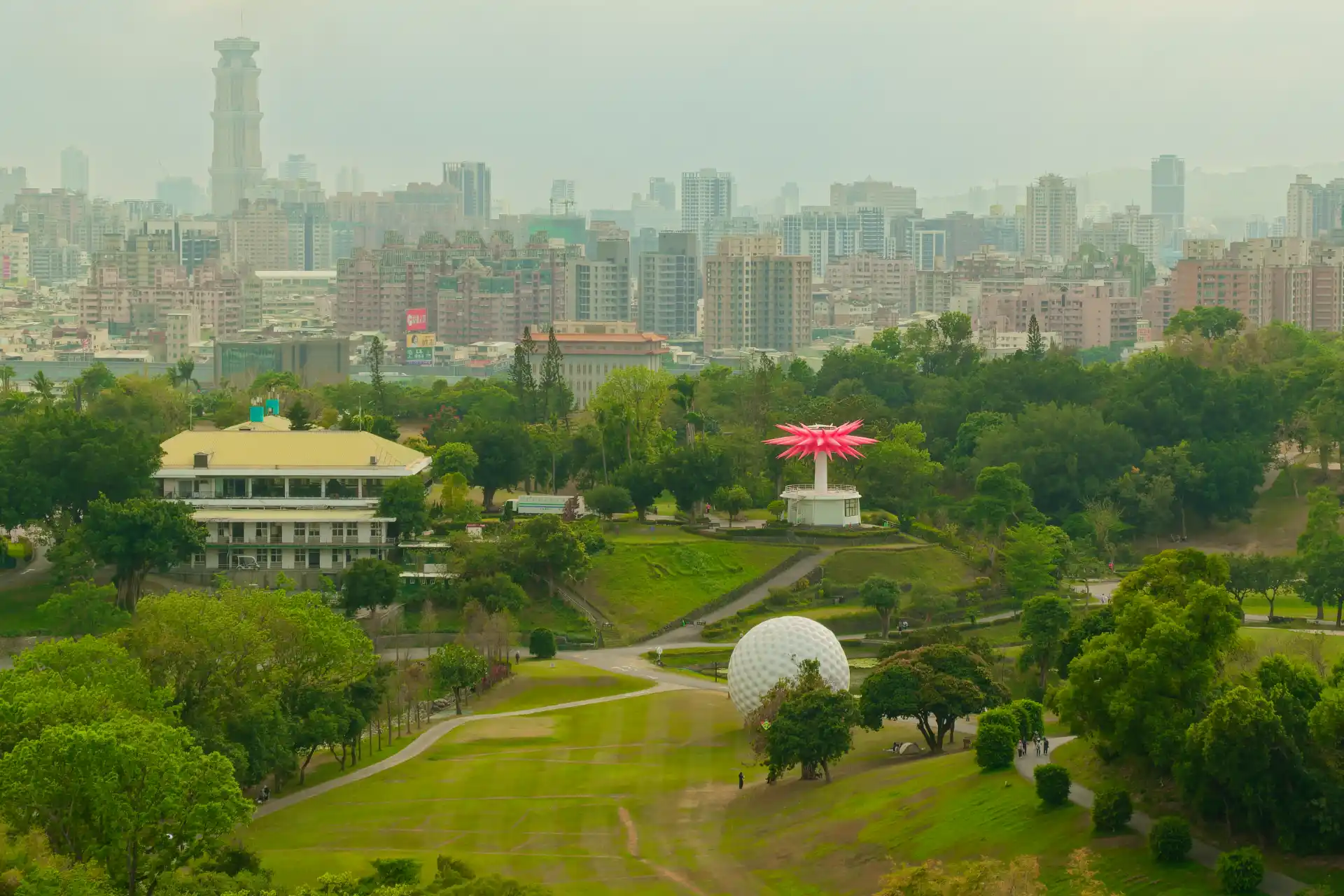 An expansive green park that looks like a golf course, including a much-larger-than-life sculpture of a golf ball, and a pink starburst-style sculpture.