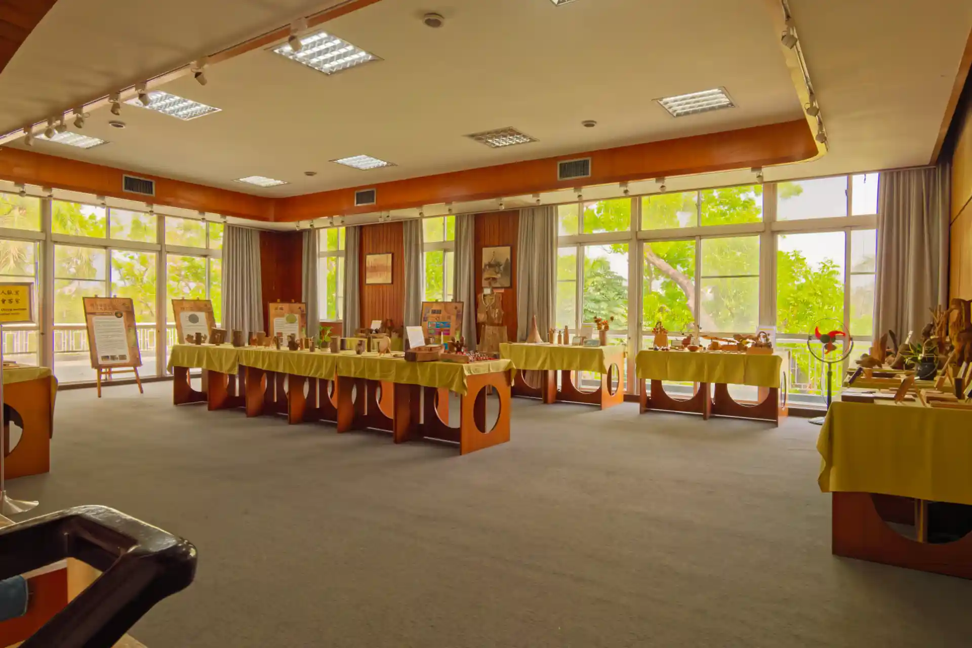 A large open room with floor-to-ceiling windows along two sides. Temporary desks have been set up around the room, with small wooden items displayed on them.