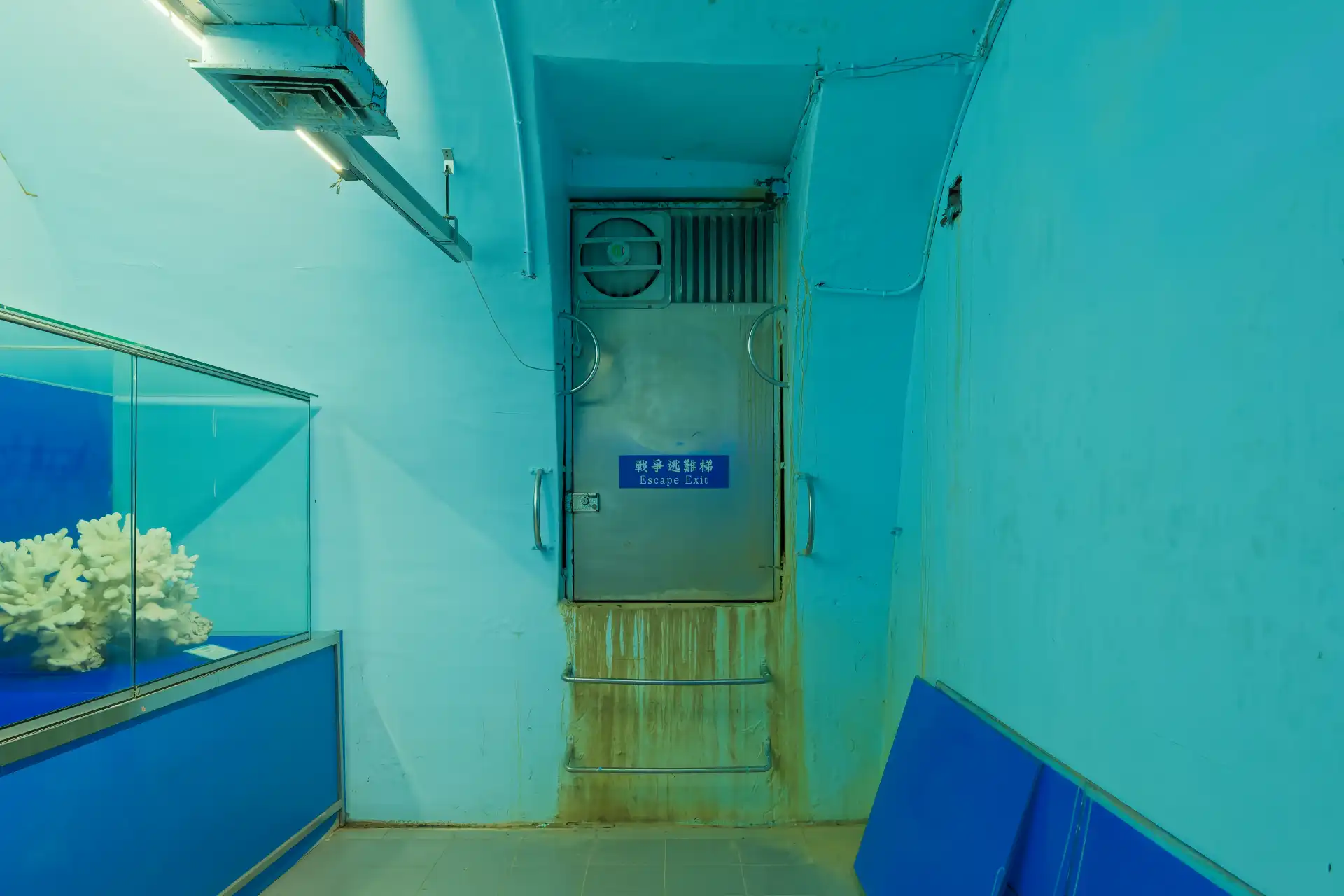 In a concrete room with an arched ceiling, a small steel door marked “Escape Exit”.