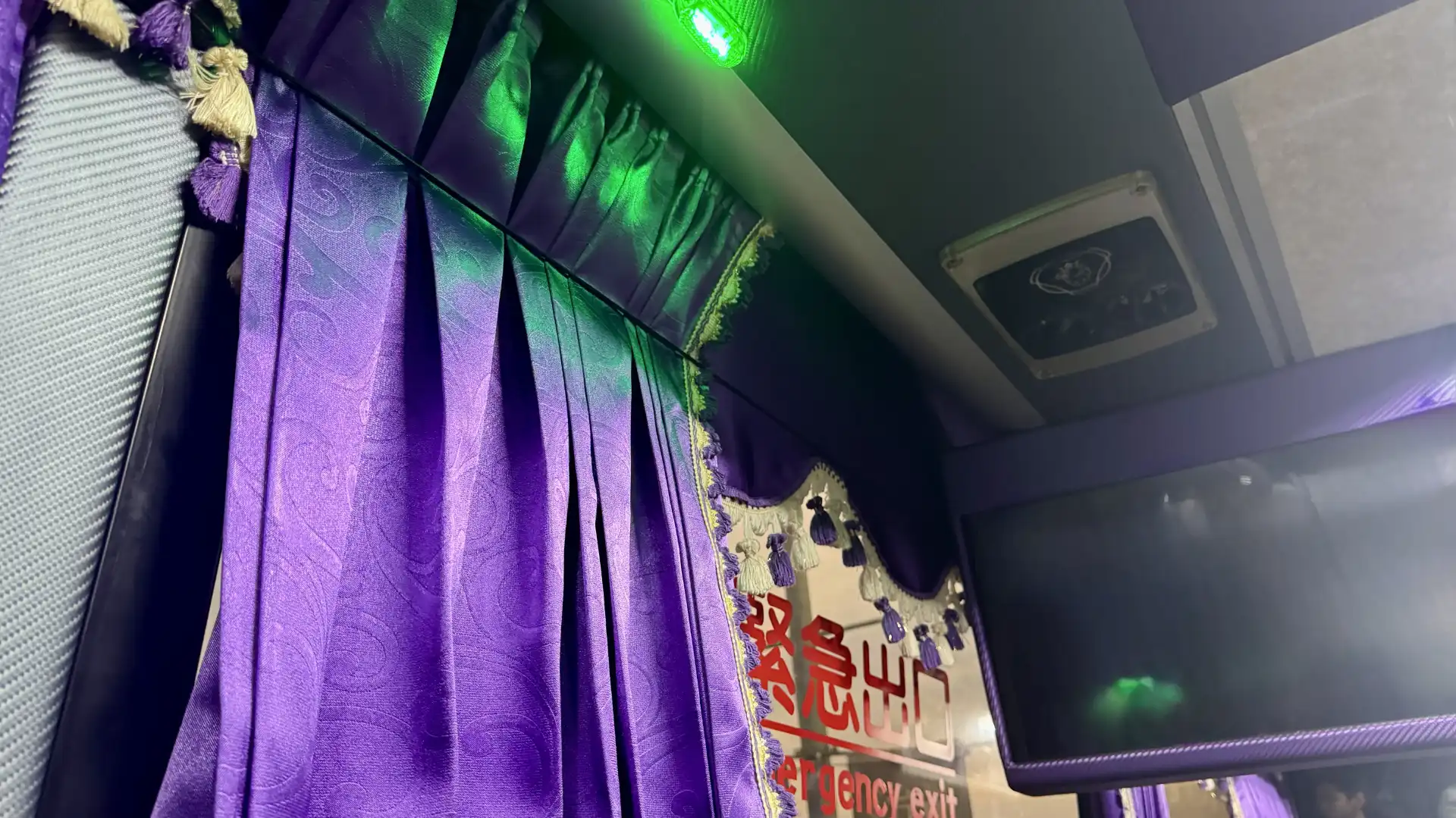 Bus interior close-up of frilly purple curtains and a neon green ceiling light.