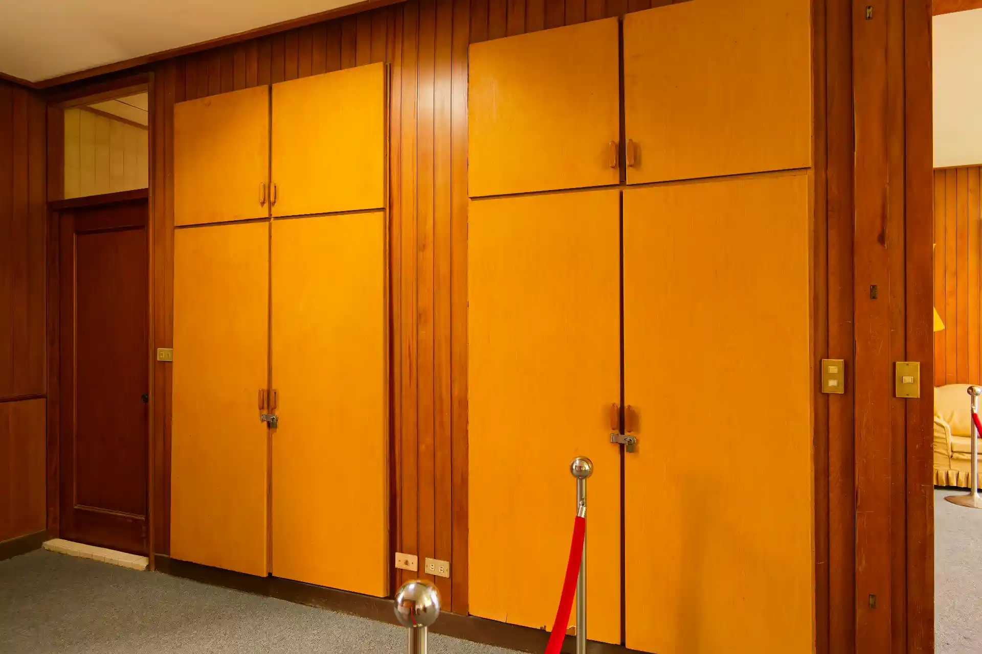 Two inbuilt double closets along one wall of a bedroom. A bathroom door is visible to the extreme left, beyond a velvet rope.