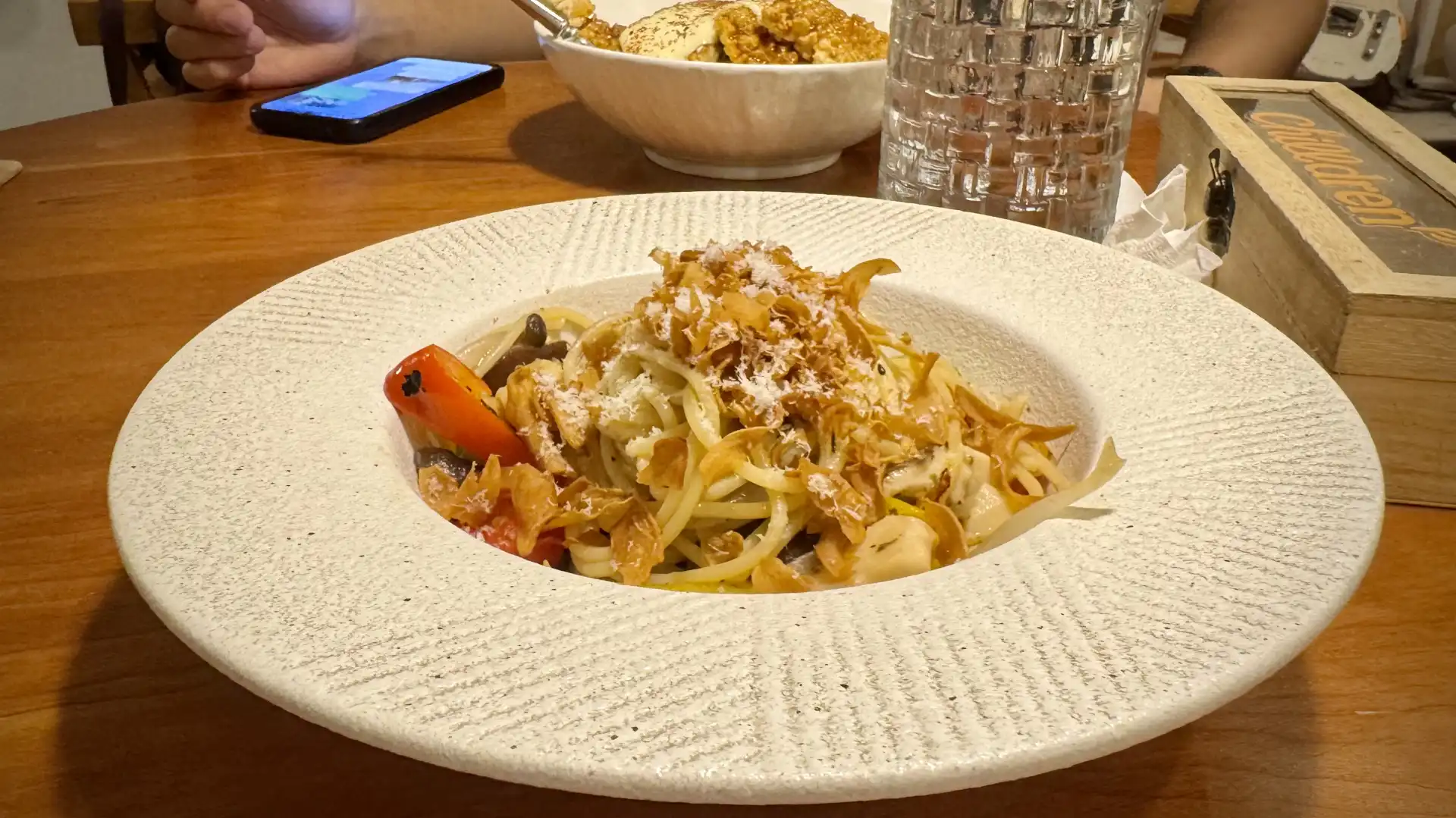 A wide-rimmed bowl containing a delicious-looking pasta dish on the table at a restaurant. Another dish, of vegetarian chicken, is just visible in the background.