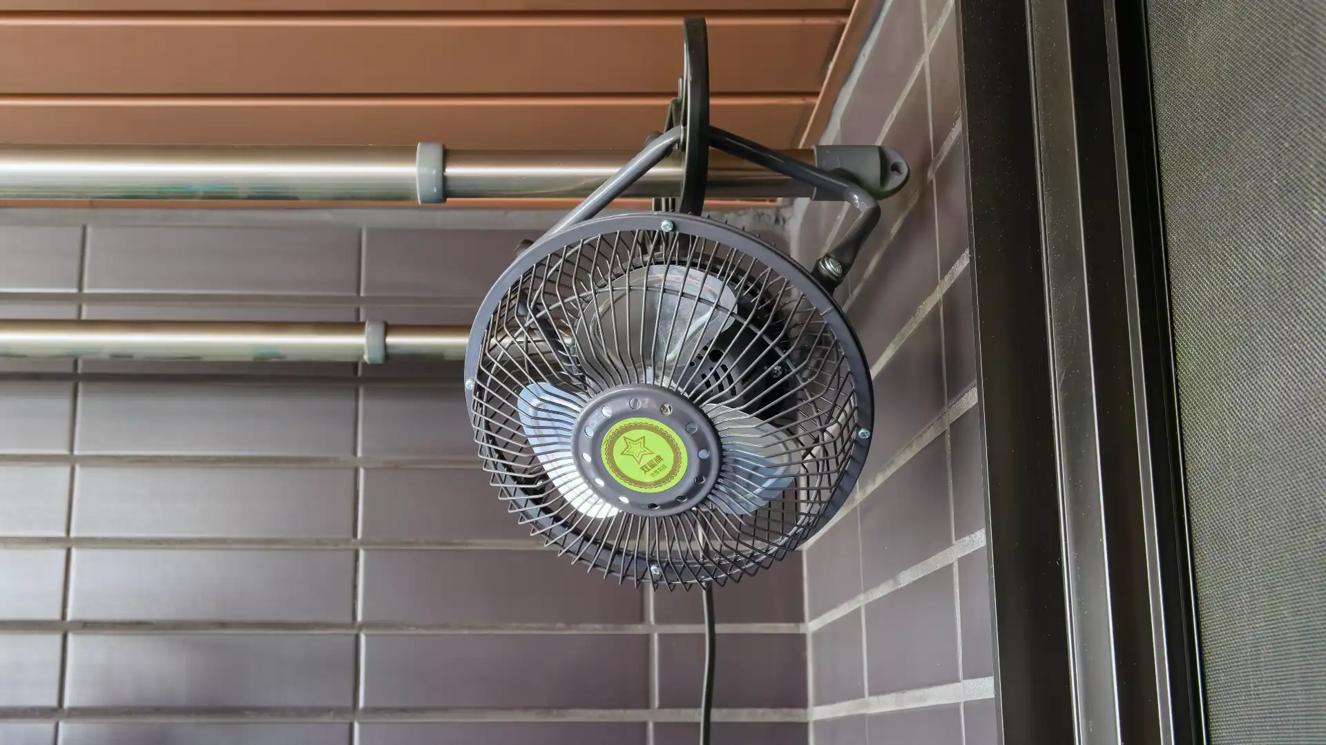 A compact electric fan hanging from a wall mount on an apartment balcony in Taiwan.