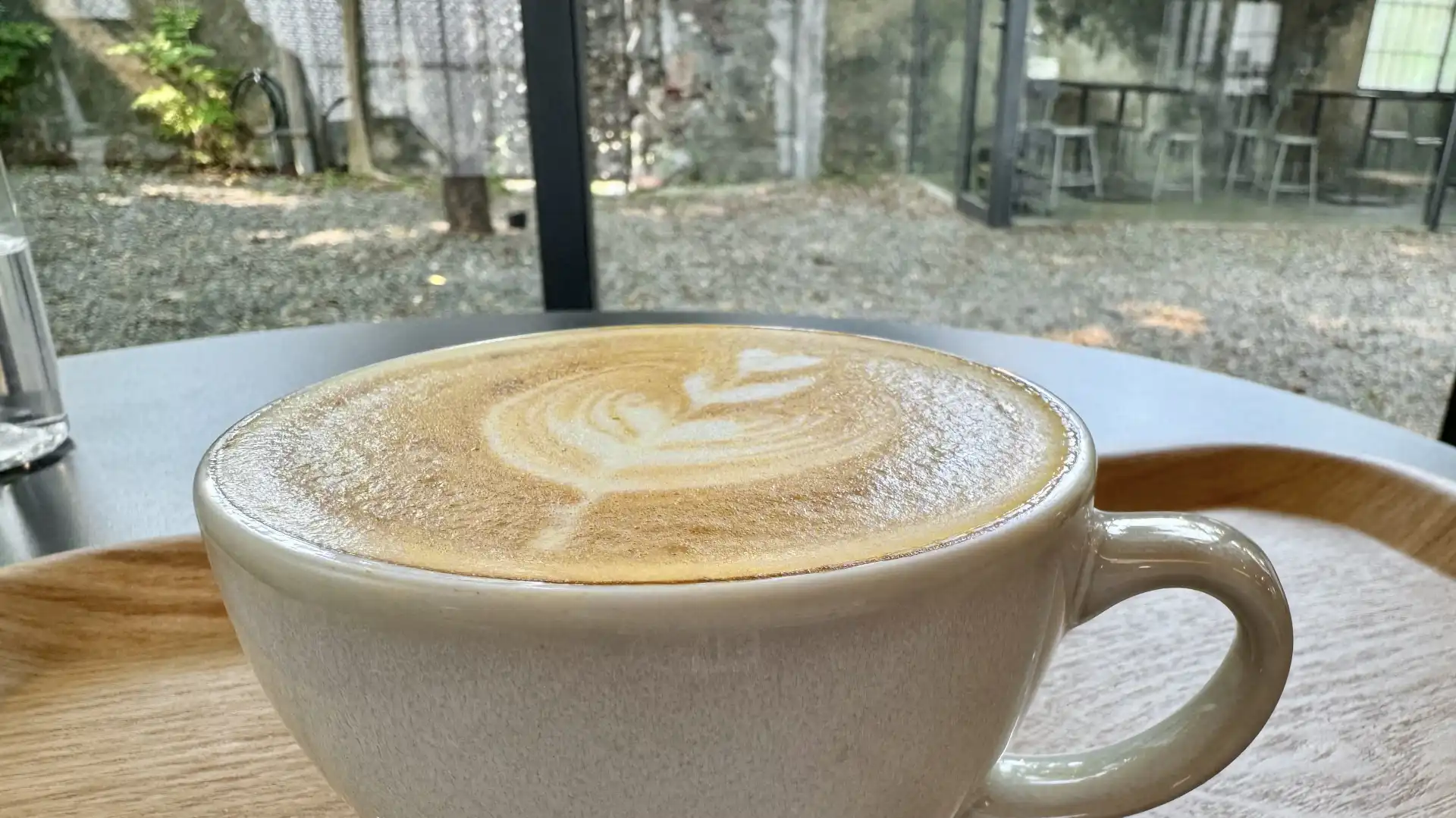 Close-up of a hot latte, with a minimalist stone garden visible through the glass wall beyond.