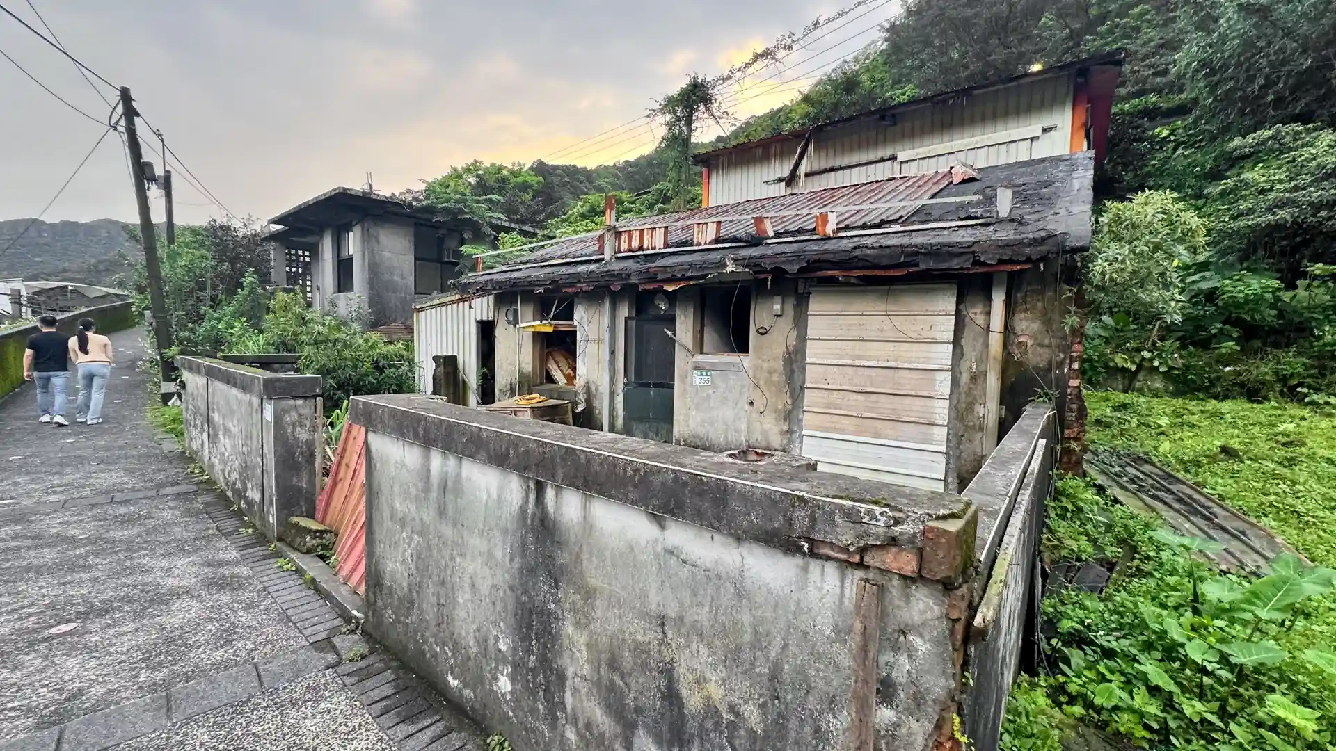 A two-level abandoned concrete building next to a hillside field at Houton Village.