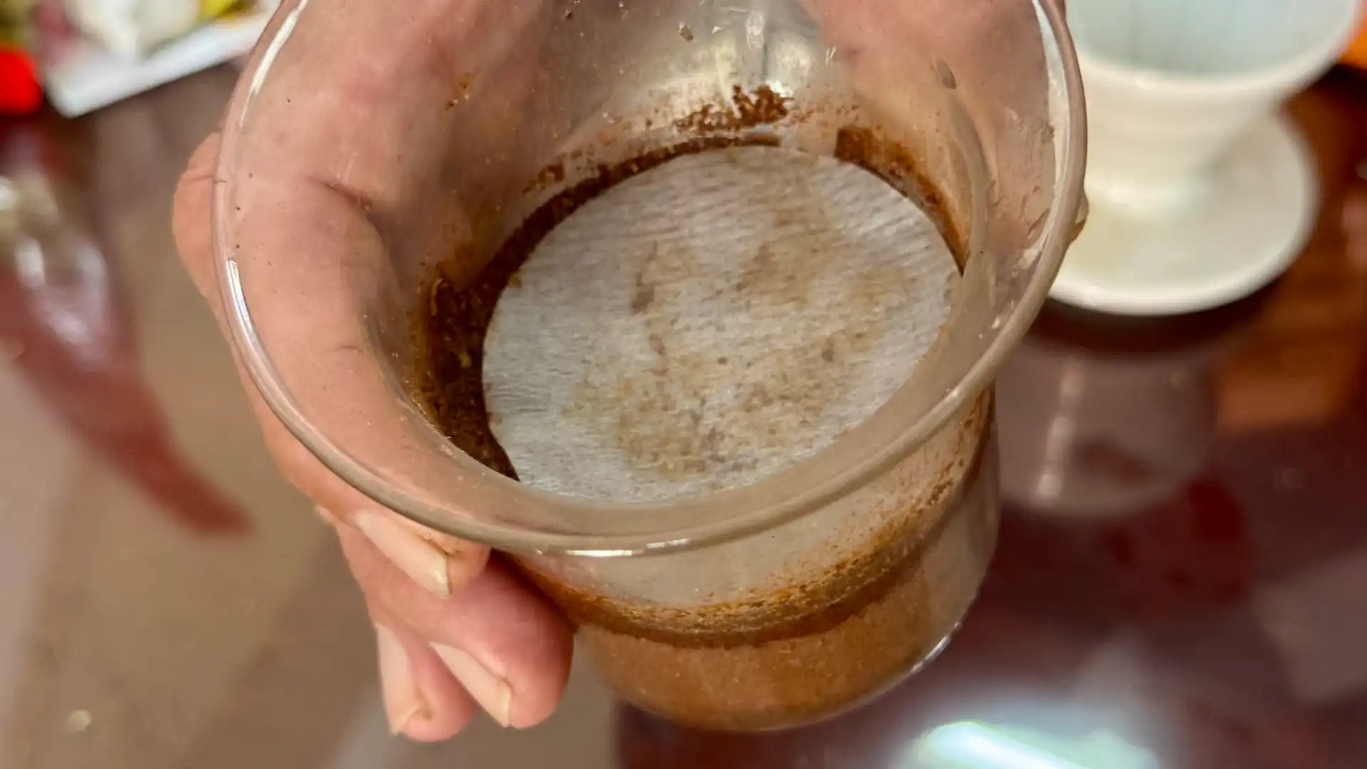 A glass brew chamber half-filled with dry coffee grounds, with a round wet piece of filter paper placed on top.