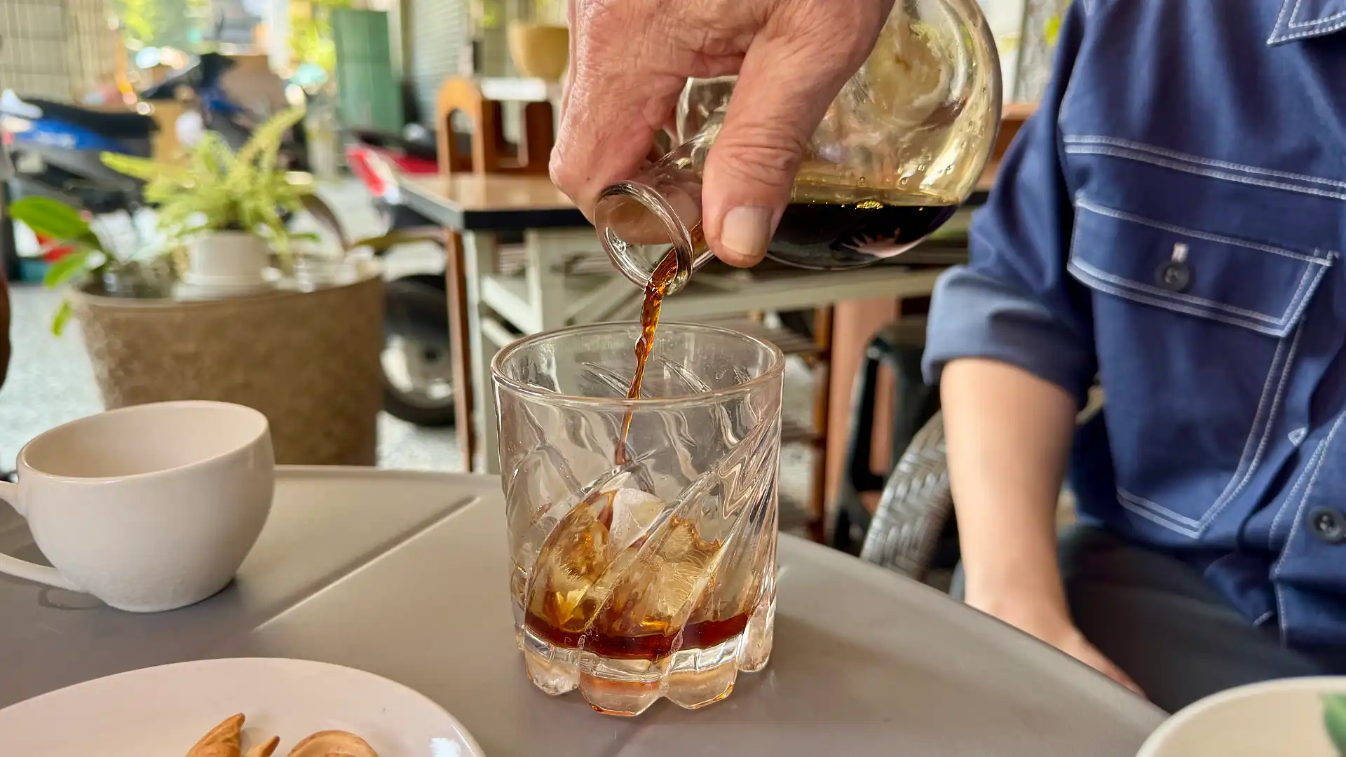 Coffee being poured from a glass carafe into a whiskey glass containing ice cubes.