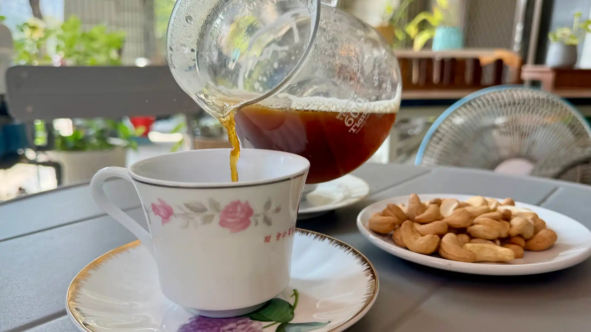 Coffee being poured from a glass carafe into an elegant teacup.