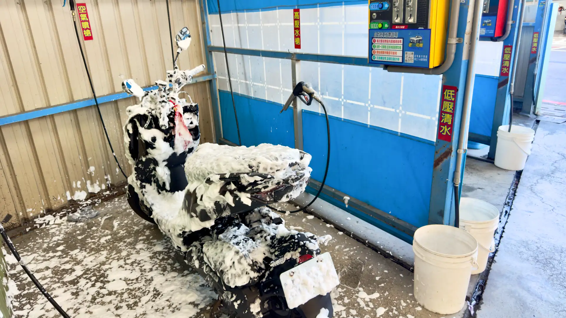 A scooter covered in foam bubbles at a Taiwanese self-service scooter wash bay.