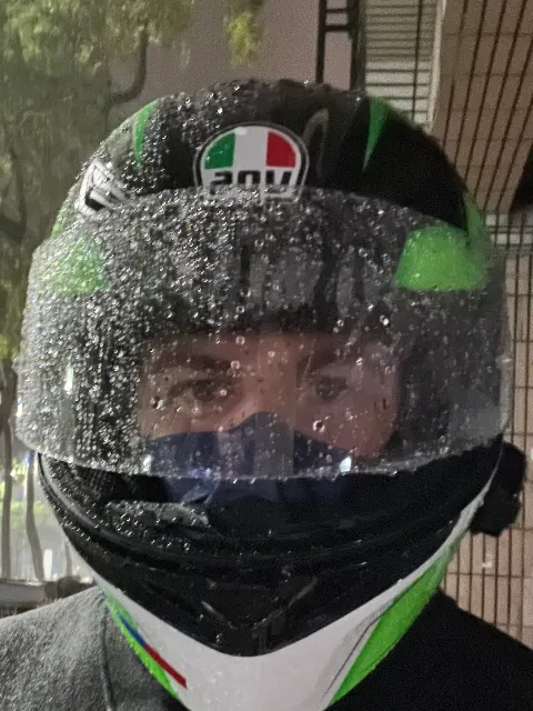 A very wet man wearing a full-face motorcycle helmet, standing on the street at night.