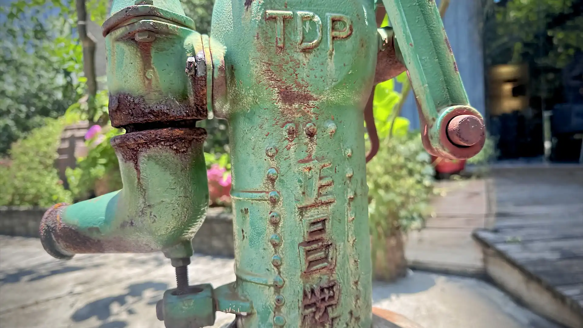 Close-up of a cast-iron water pump, painted a faded green and slightly rusted, on an urban Taiwan roadside.