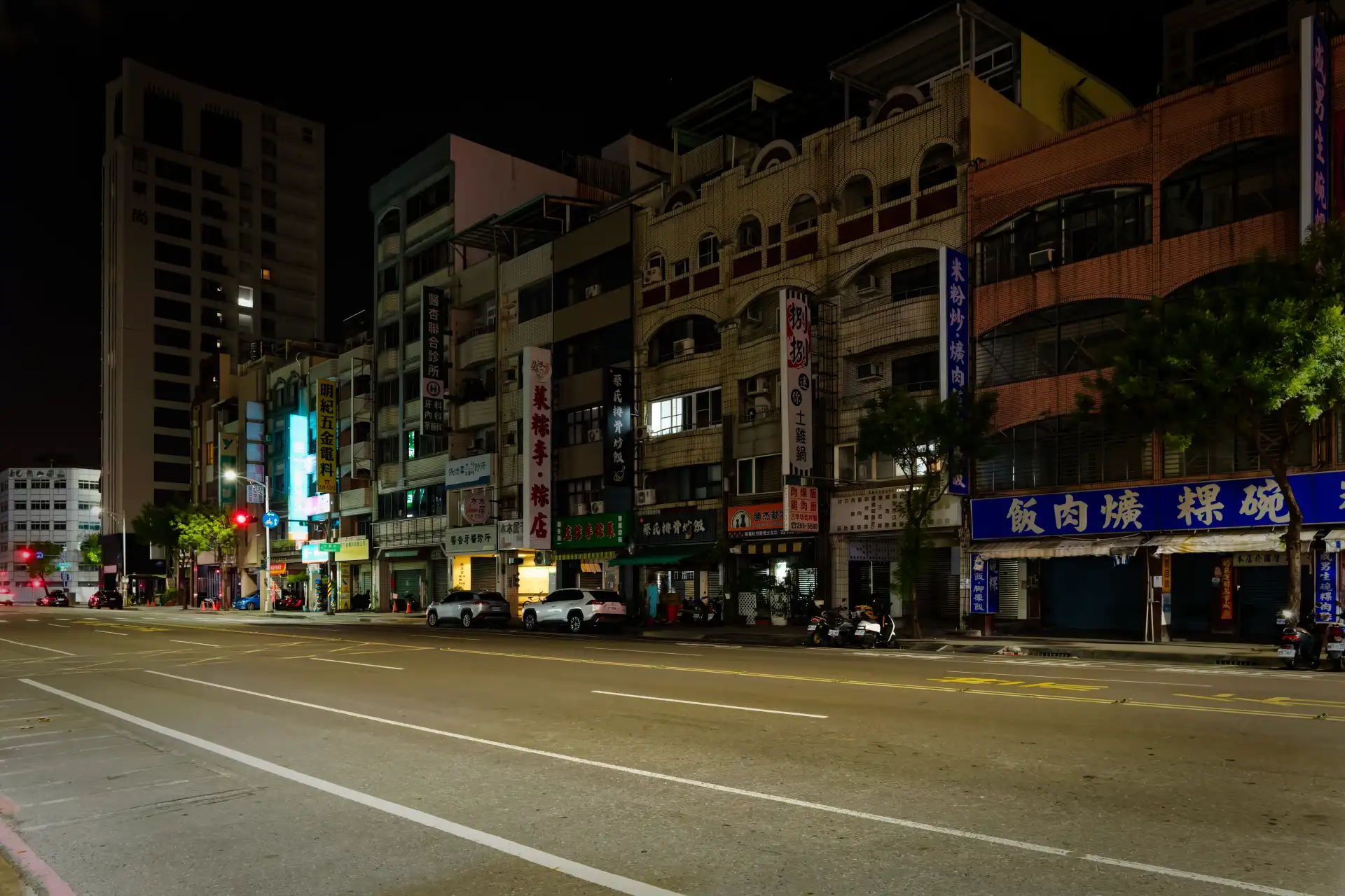 A row of dense 4-to-5-story townhouses and apartment buildings on a wide road in Kaohsiung, Taiwan, at night.