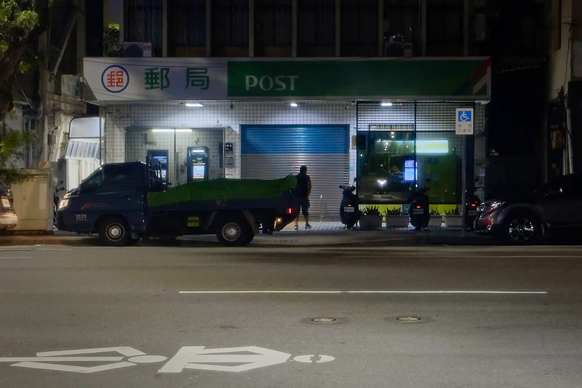 A man walking past a branch of Chunghwa Post at night.