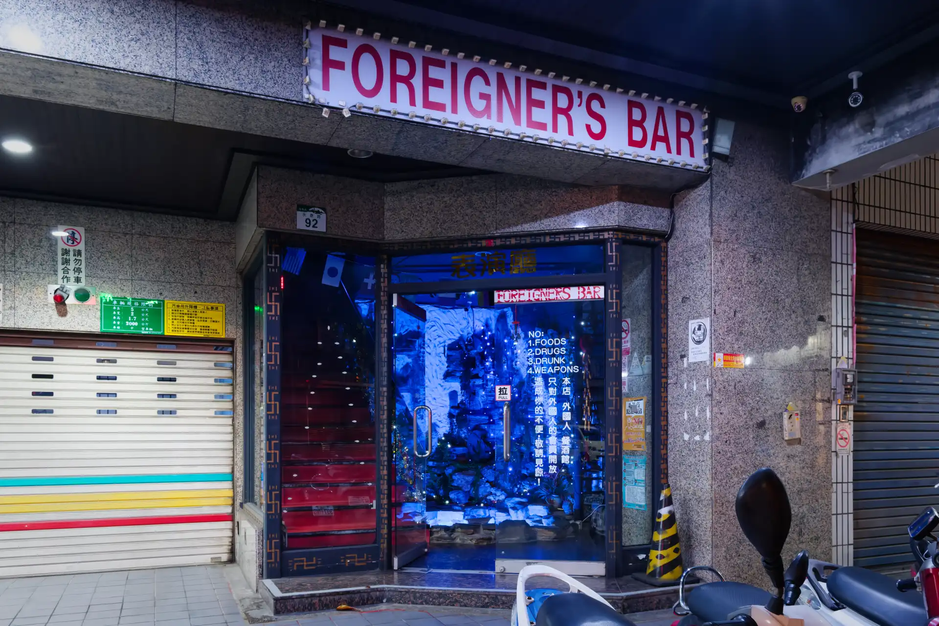 Glass doors leading to a red staircase, under a sign that reads “FOREIGNER’S BAR”.