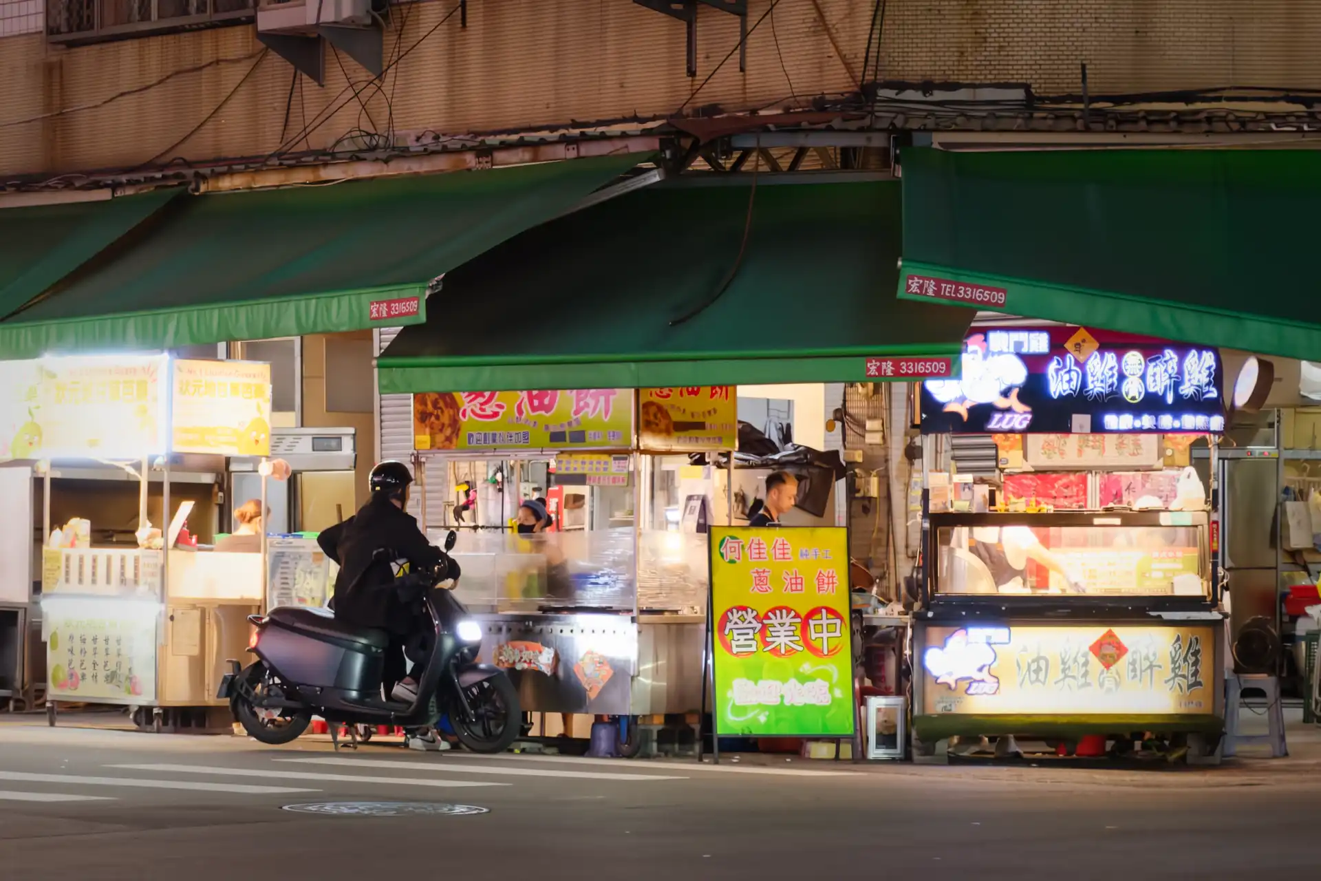 A person sitting on a scooter waiting at a green onion pancake stall at Lingya Night Market in Kaohsiung, Taiwan.