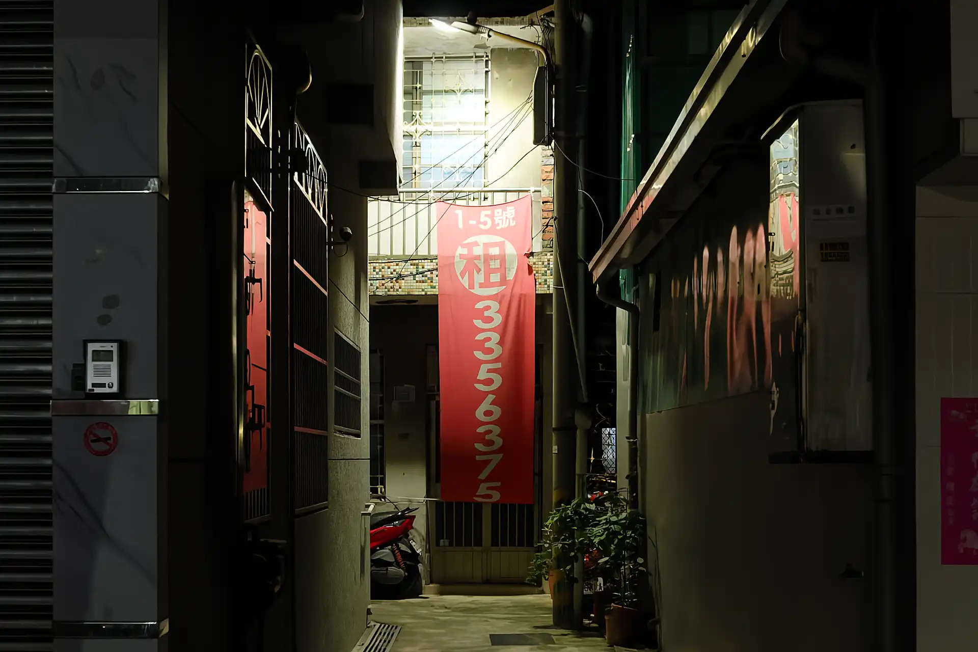An advertising banner with a phone number hangs from the second floor of a house in a clean, narrow alleyway in Kaohsiung, Taiwan.