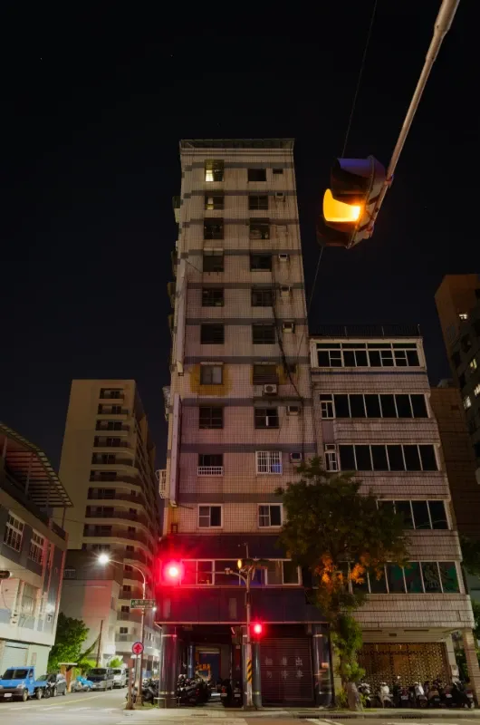 A narrow 12-story apartment building at night. It has a metal roof shading the roof garden.