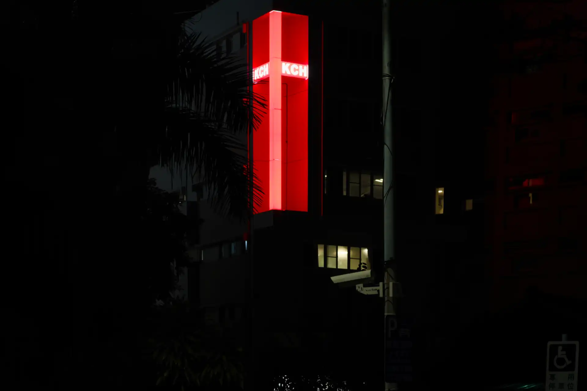 A three-story tall cross shape integrated into the corner of Kaohsiung Christian Hospital, illuminated red at night.