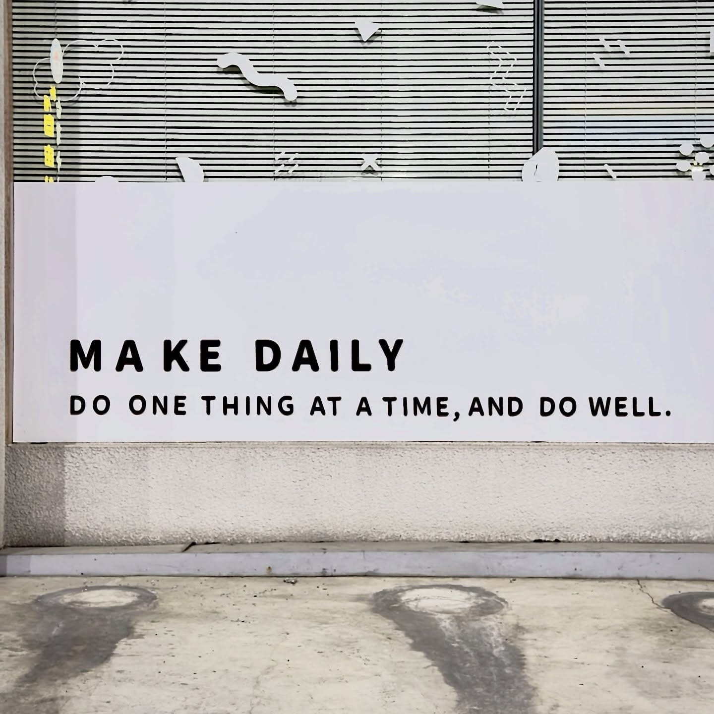 Close-up of a sign on a business which reads “MAKE DAILY / Do one thing at a time, and do well”.