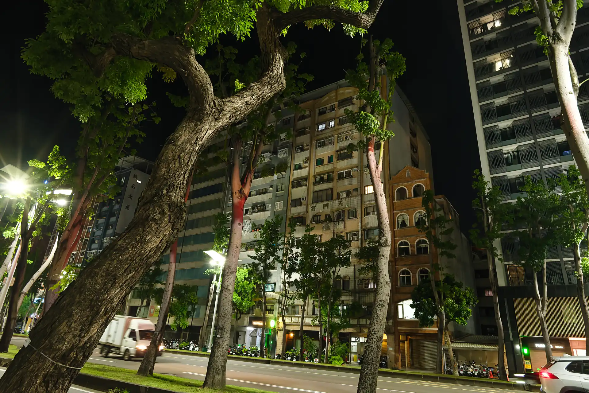 A dense row of 5-to-15-story apartment buildings on a wide tree-lined street in Kaohsiung, Taiwan, at night.