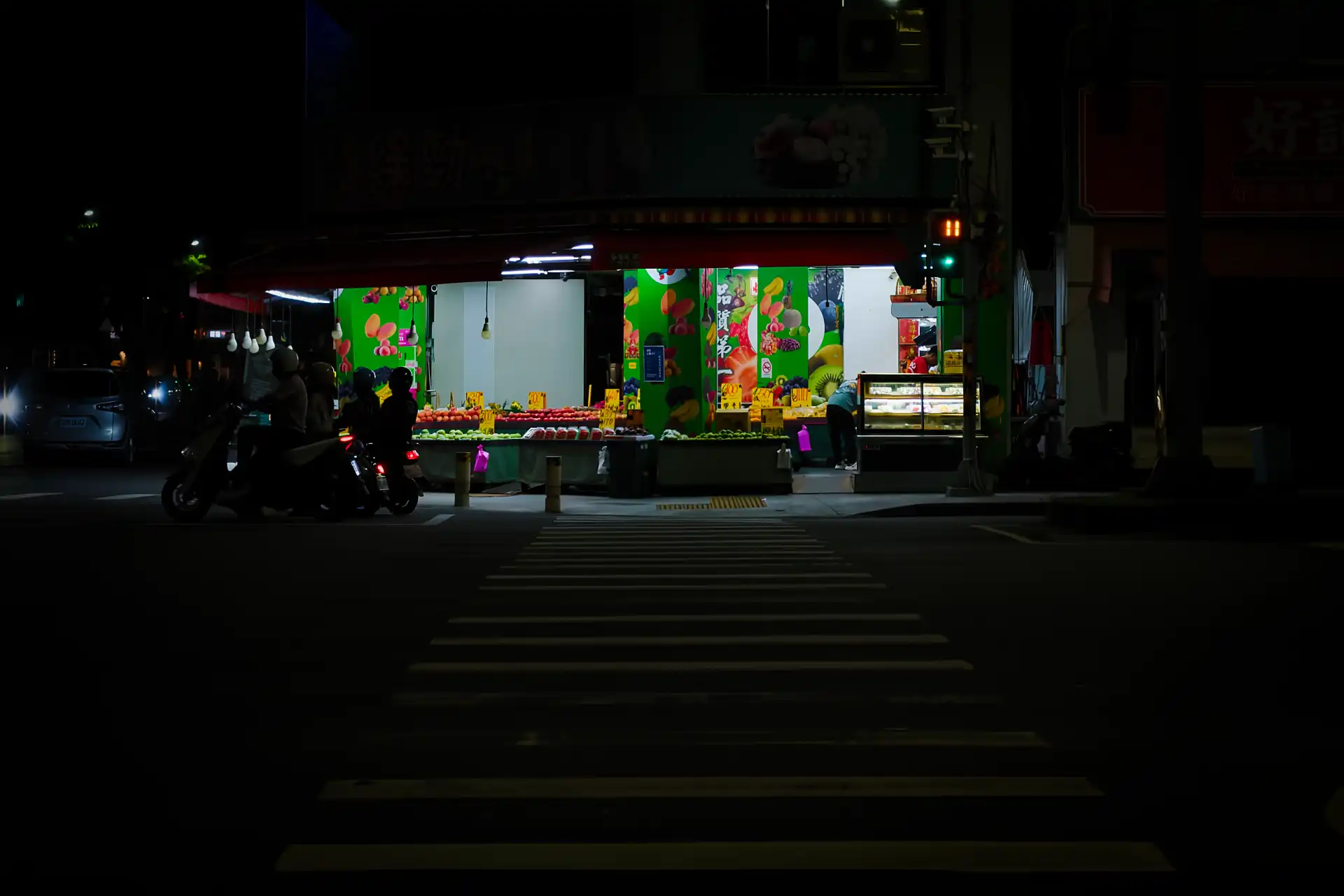 A fruit store open at night, in a photo taken from across a dark street.