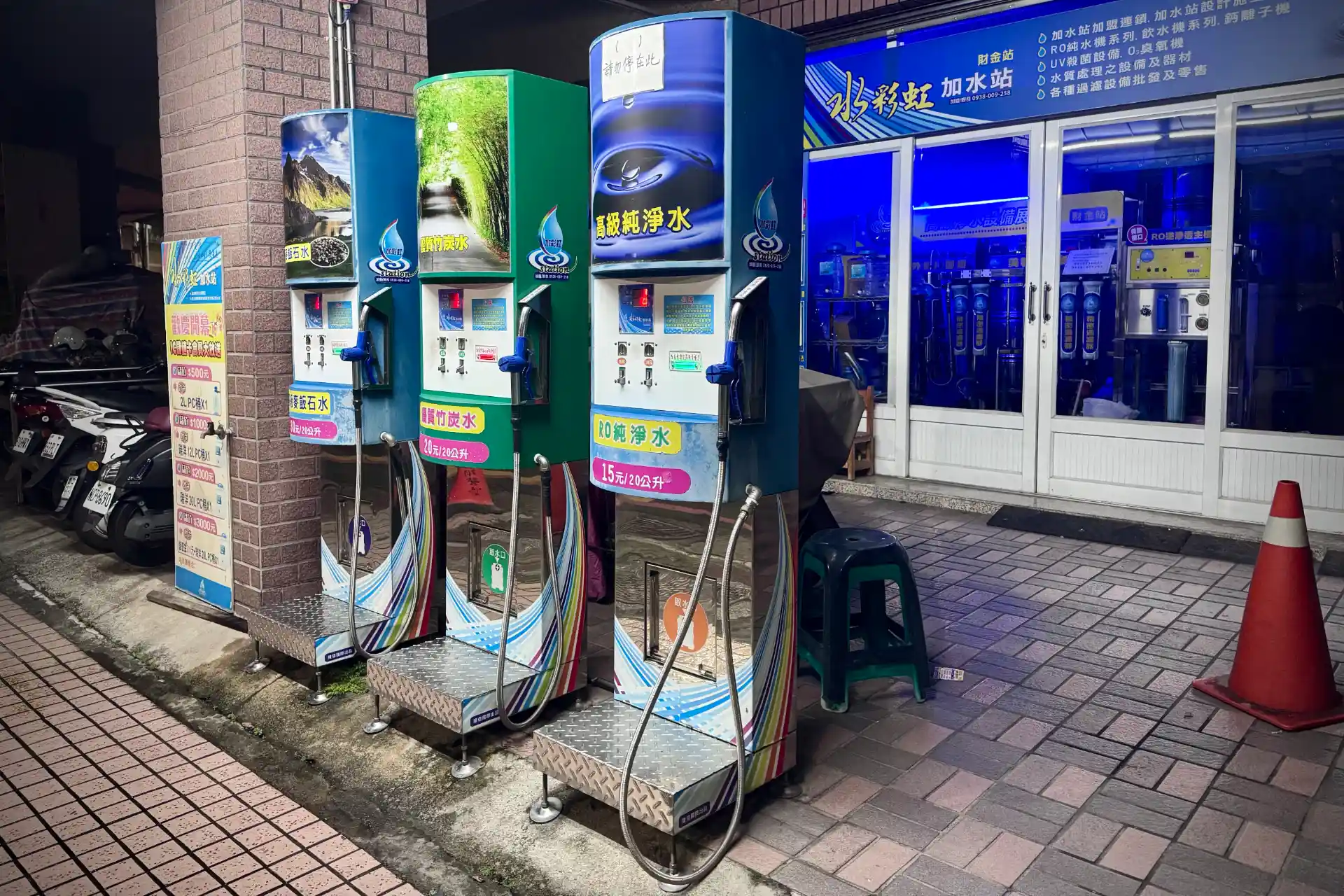 Three self-service water dispensing machines on a sidewalk in Kaohsiung, Taiwan. They look similar to petrol bowsers, with hand-held nozzles attached to long hoses.