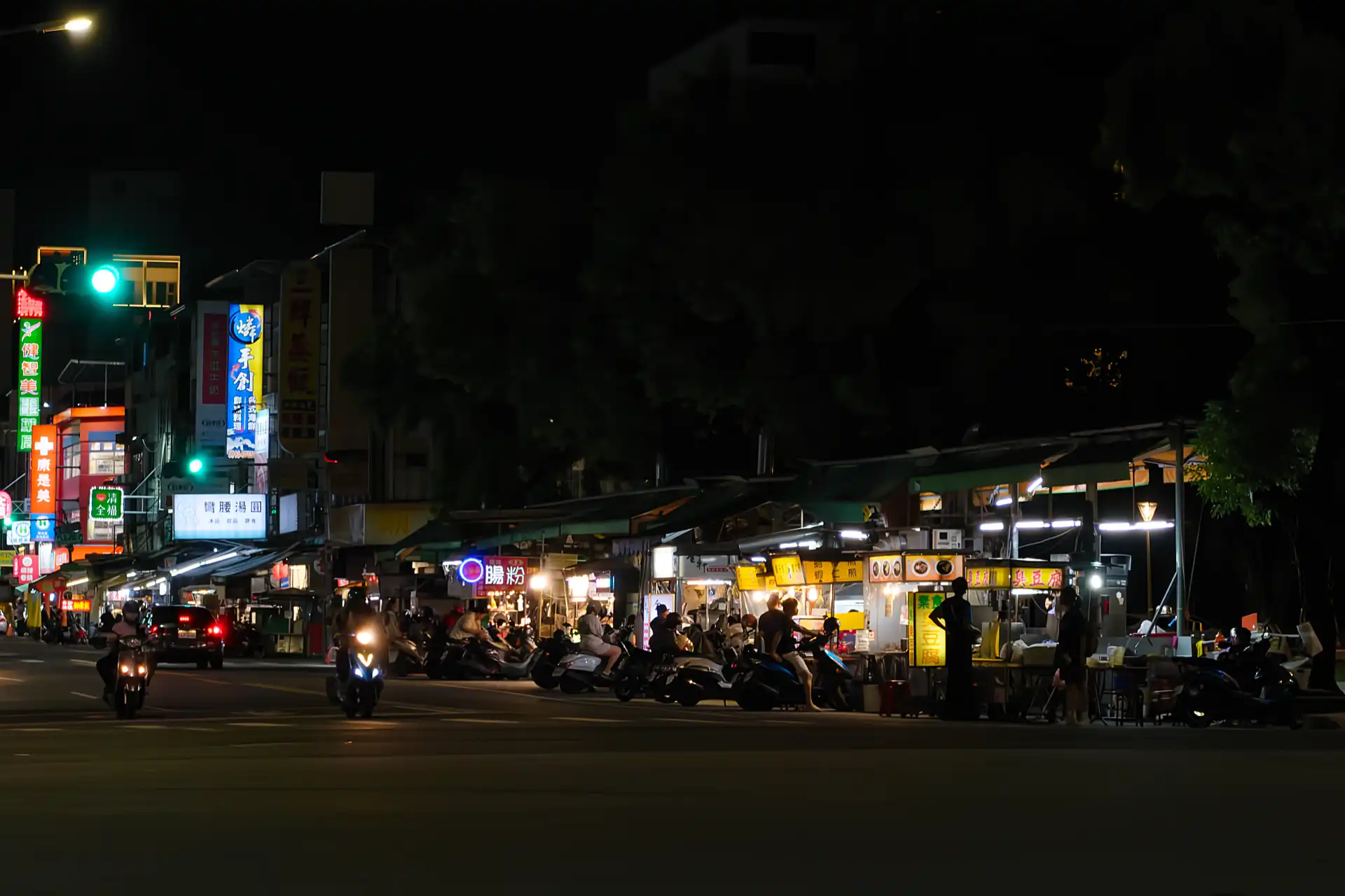 Nighttime view of Ziqiang Night Market in Kaohsiung, Taiwan. People on scooters are lined up outside the stalls.