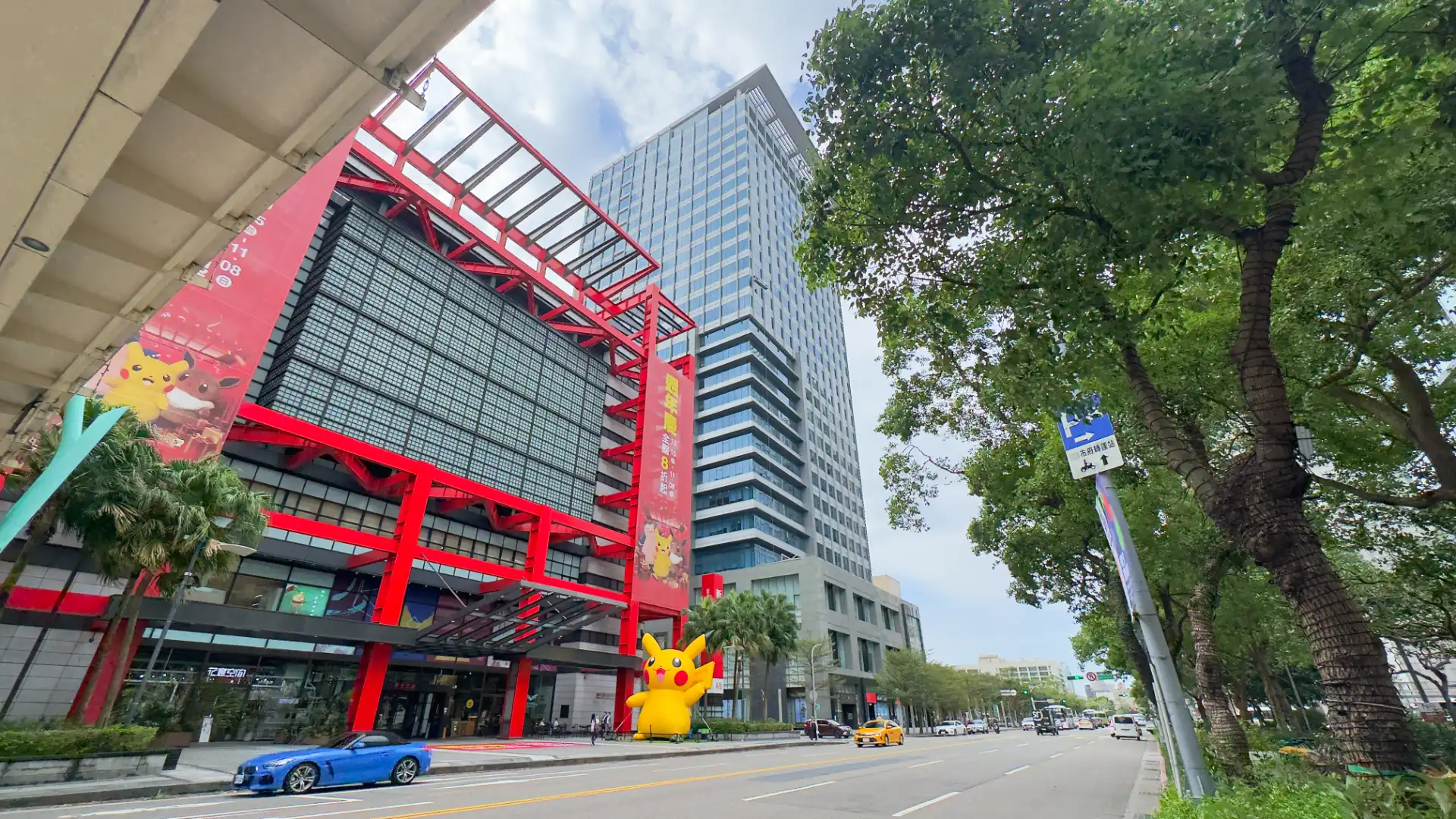 A wide, leafy street in Taipei, with a giant inflatable Pikachu (Pokemon) sculpture outside a tall modern office tower.