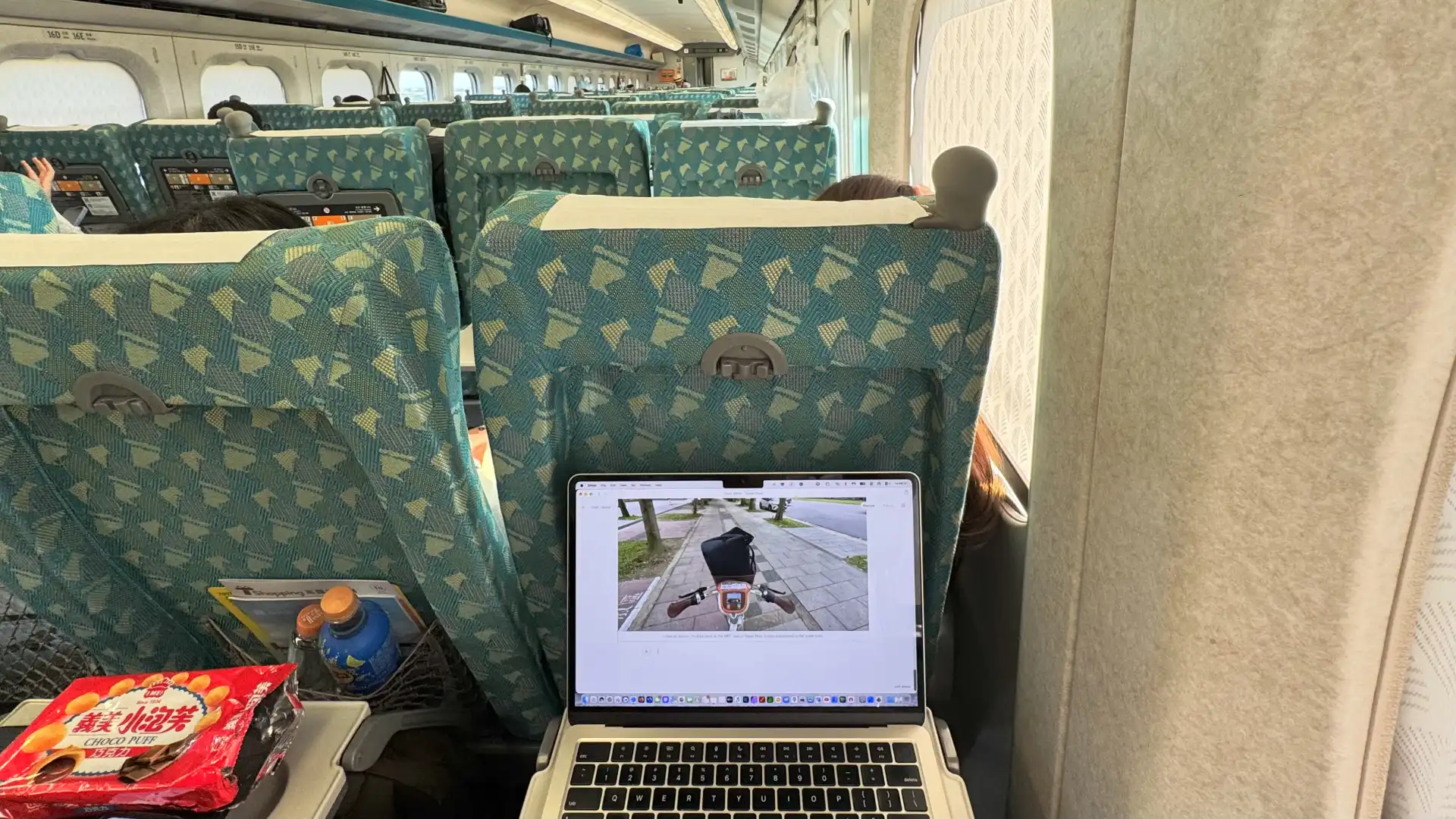 Point-of-view shot of a MacBook Air in use in a Taiwan High Speed Rail car, on the route from Taipei to Kaoshiung. The open laptop displays a blog editing page that shows the previous YouBike photo from this post on the Taiwan Quest blog.
