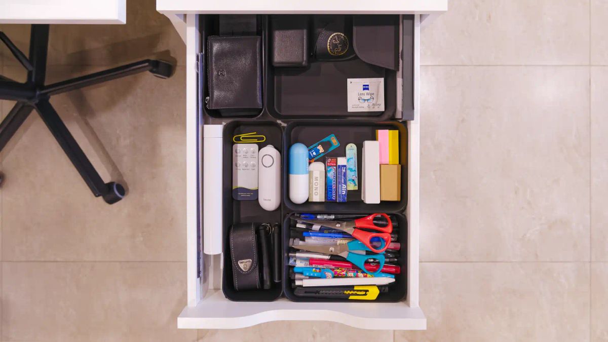 An open office drawer with stationery items in organizer trays.