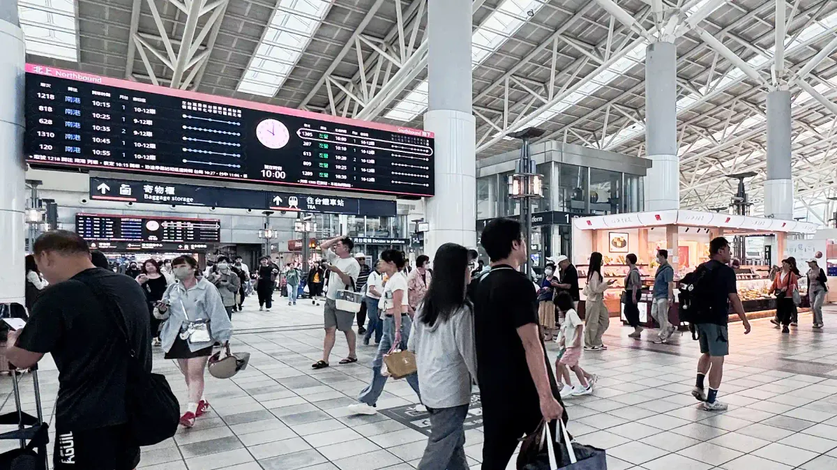 Wide-angle interior shot of people walking past a departures board at Zuoying High Speed Rail Station.