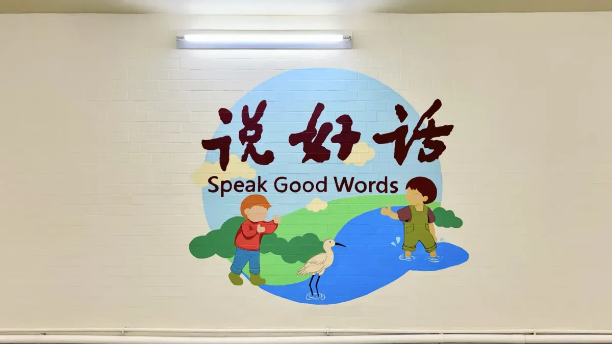 A mural showing two boys giving thumbs up beneath the English text “Speak Good Words”.