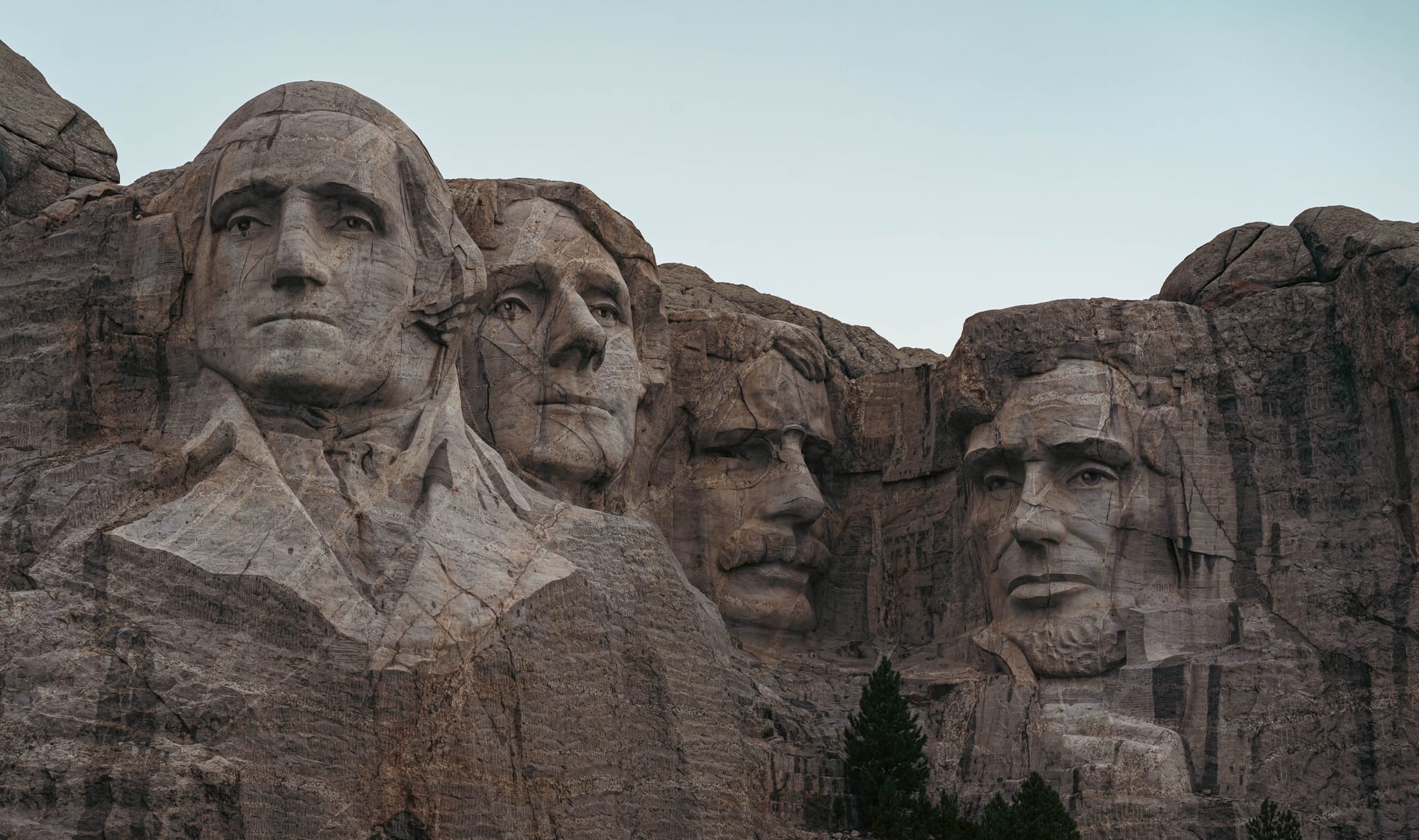 Wide view of all four presidential sculptures carved into Mount Rushmore above ponderosa pine forest.
