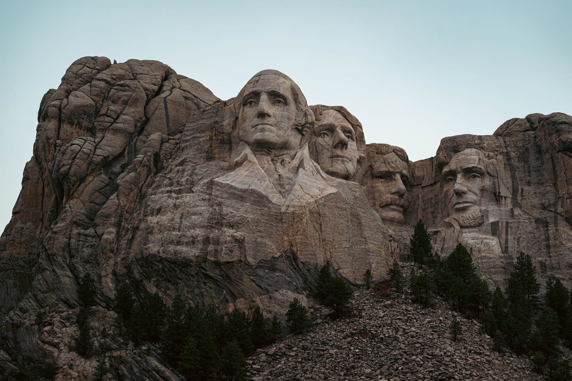 Mount Rushmore's four presidential faces rising above granite talus and ponderosa pine in the Black Hills.