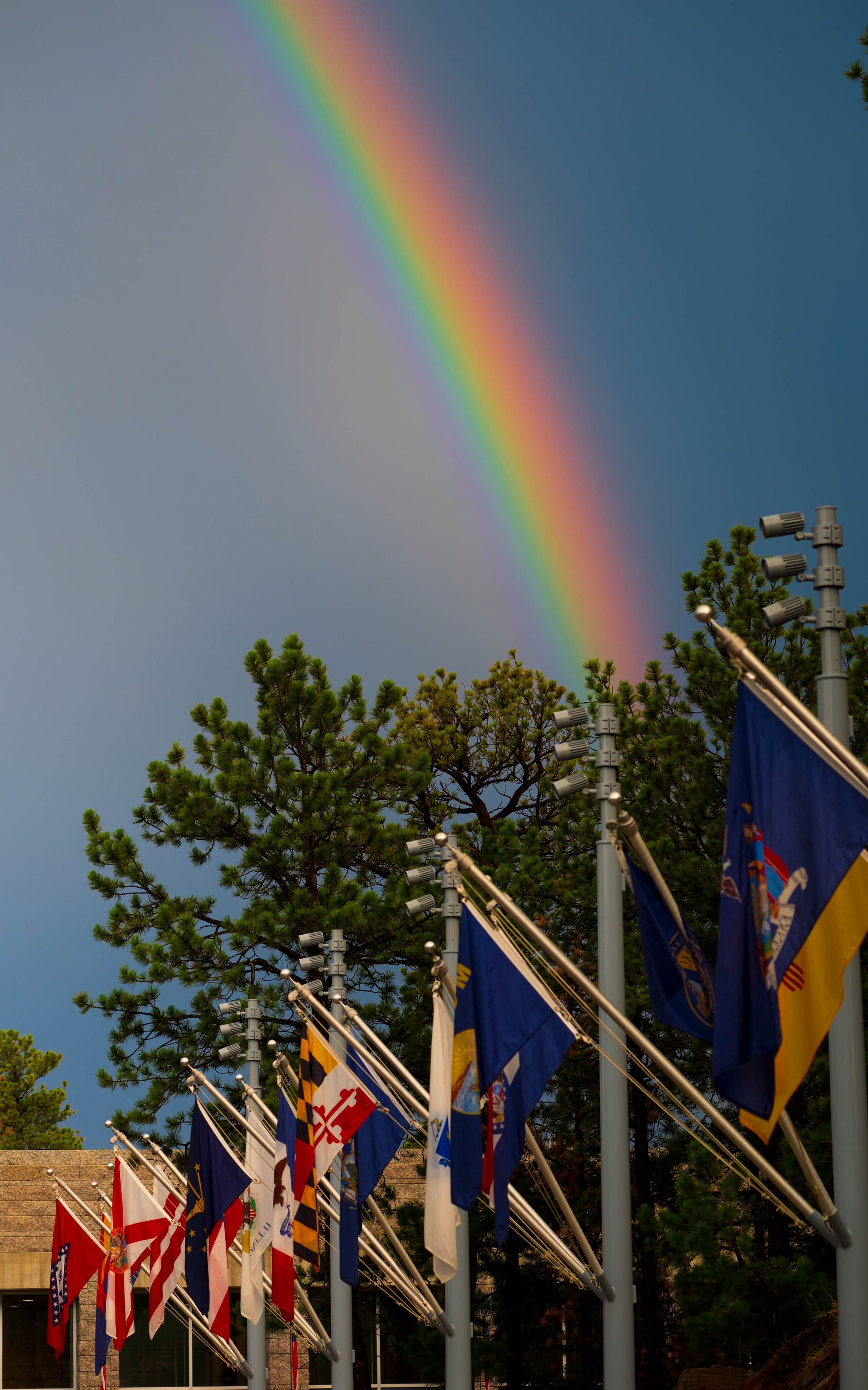 Bright rainbow arching above the Avenue of Flags at Mount Rushmore National Memorial.