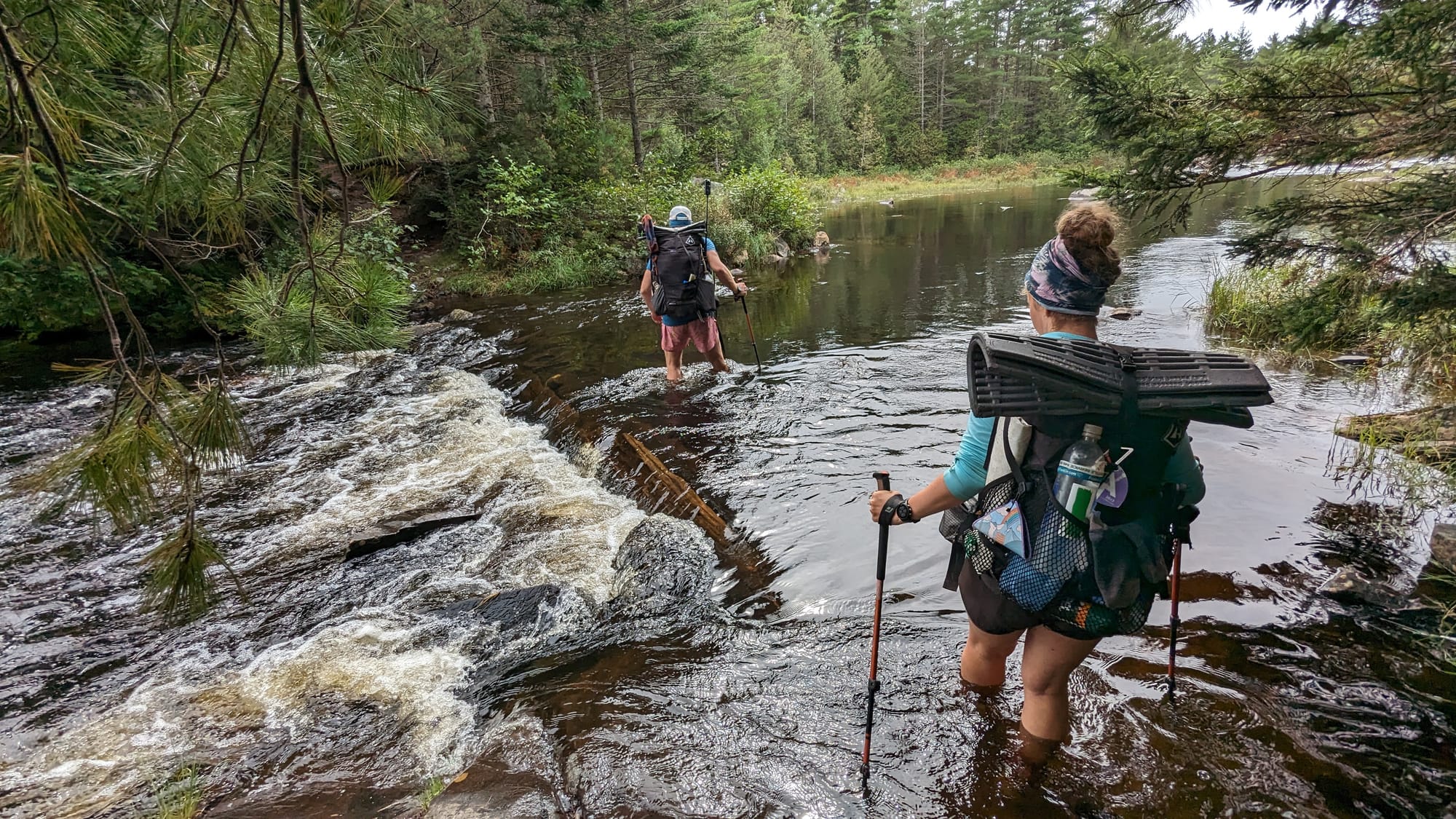 Backpackers using a rope to move gear across a high-water river crossing.