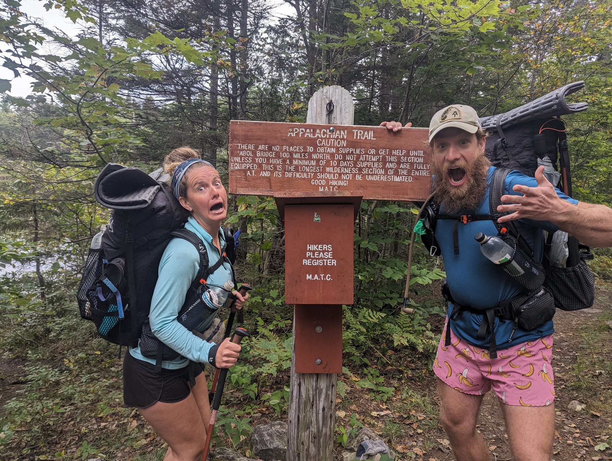 Brandon and Sunshine posing beside the Appalachian Trail warning sign at the entrance to Maine's 100-Mile Wilderness.