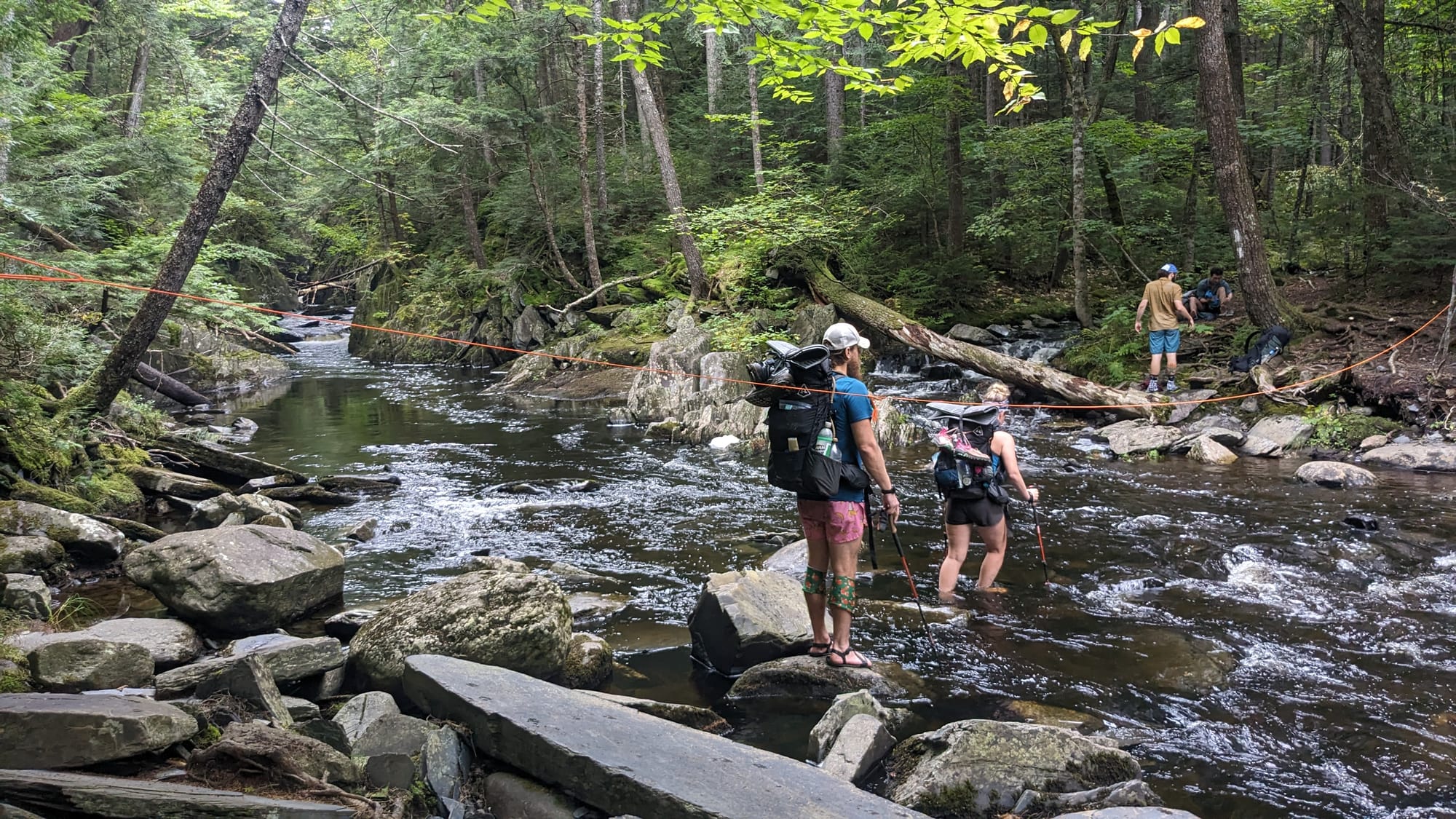 Thru-hikers carefully crossing a rocky stream swollen by recent rain.