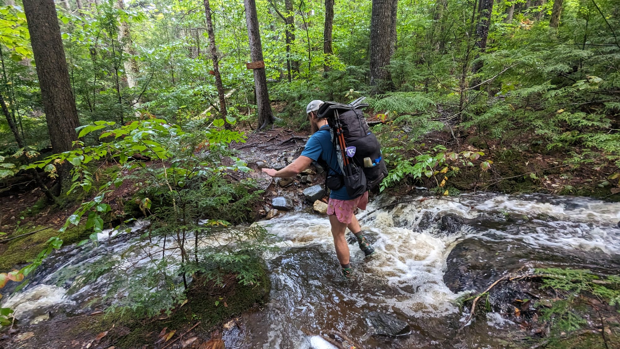 Backpacker crossing a rushing forest cascade during the 100-Mile Wilderness.