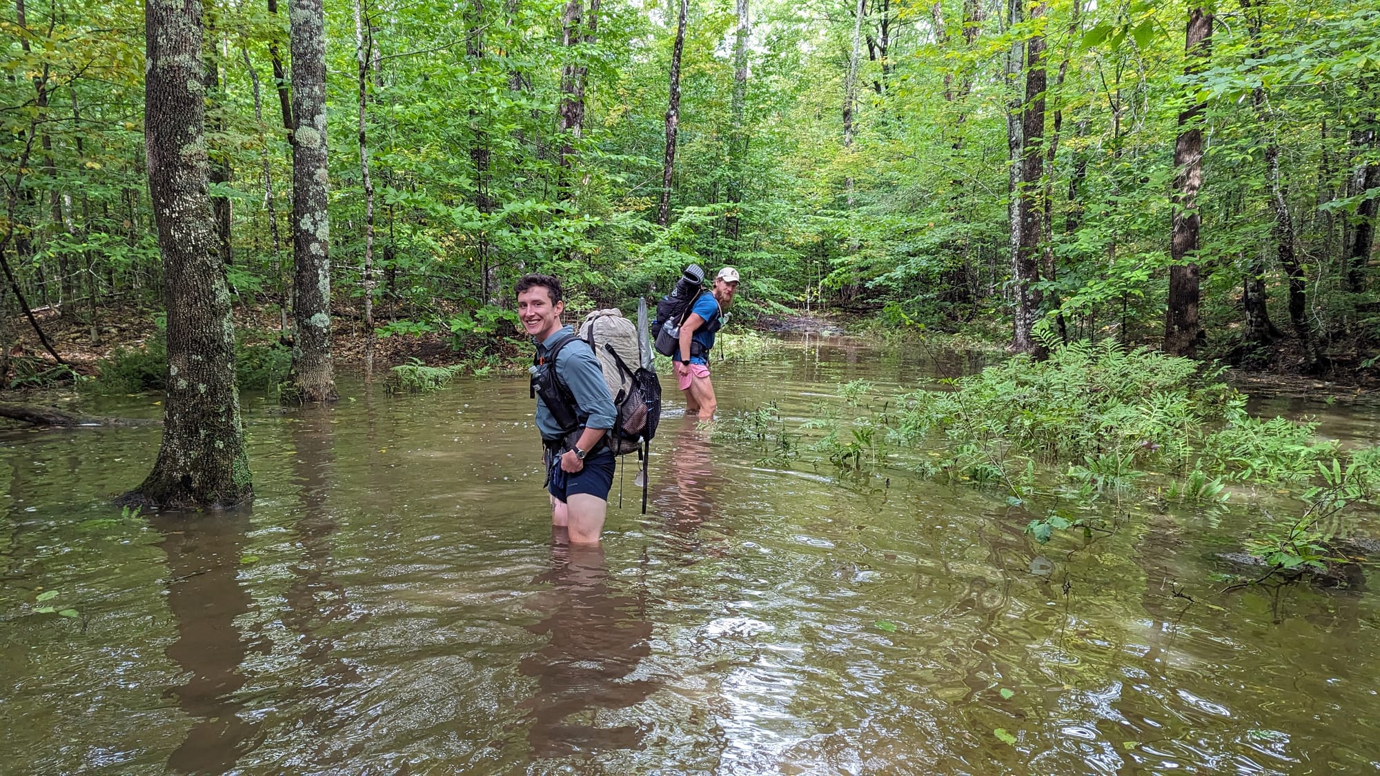 Backpackers wading knee-deep through floodwater covering the Appalachian Trail.