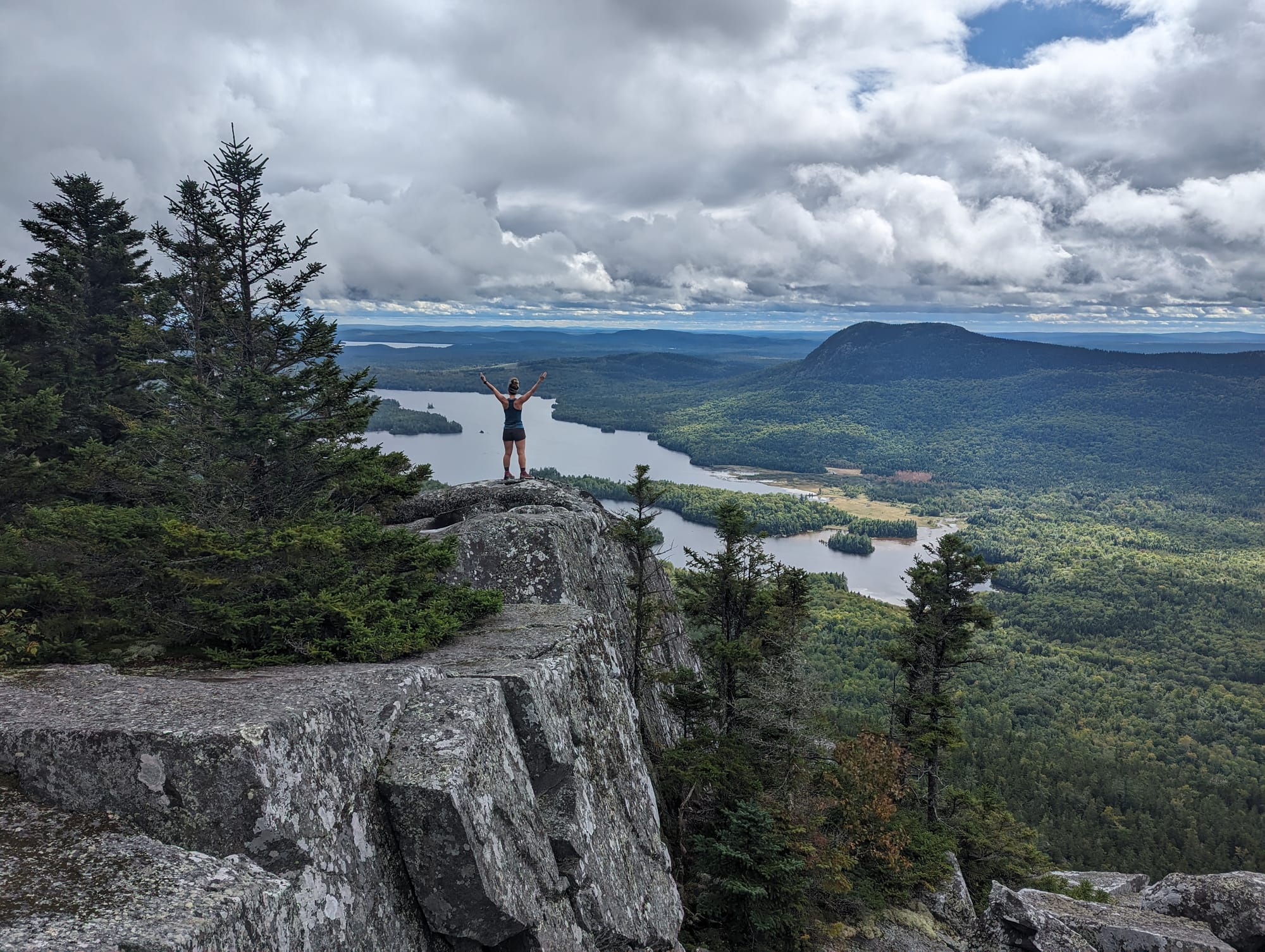 Backpacker standing on a granite overlook above lakes and dense forest near Katahdin.