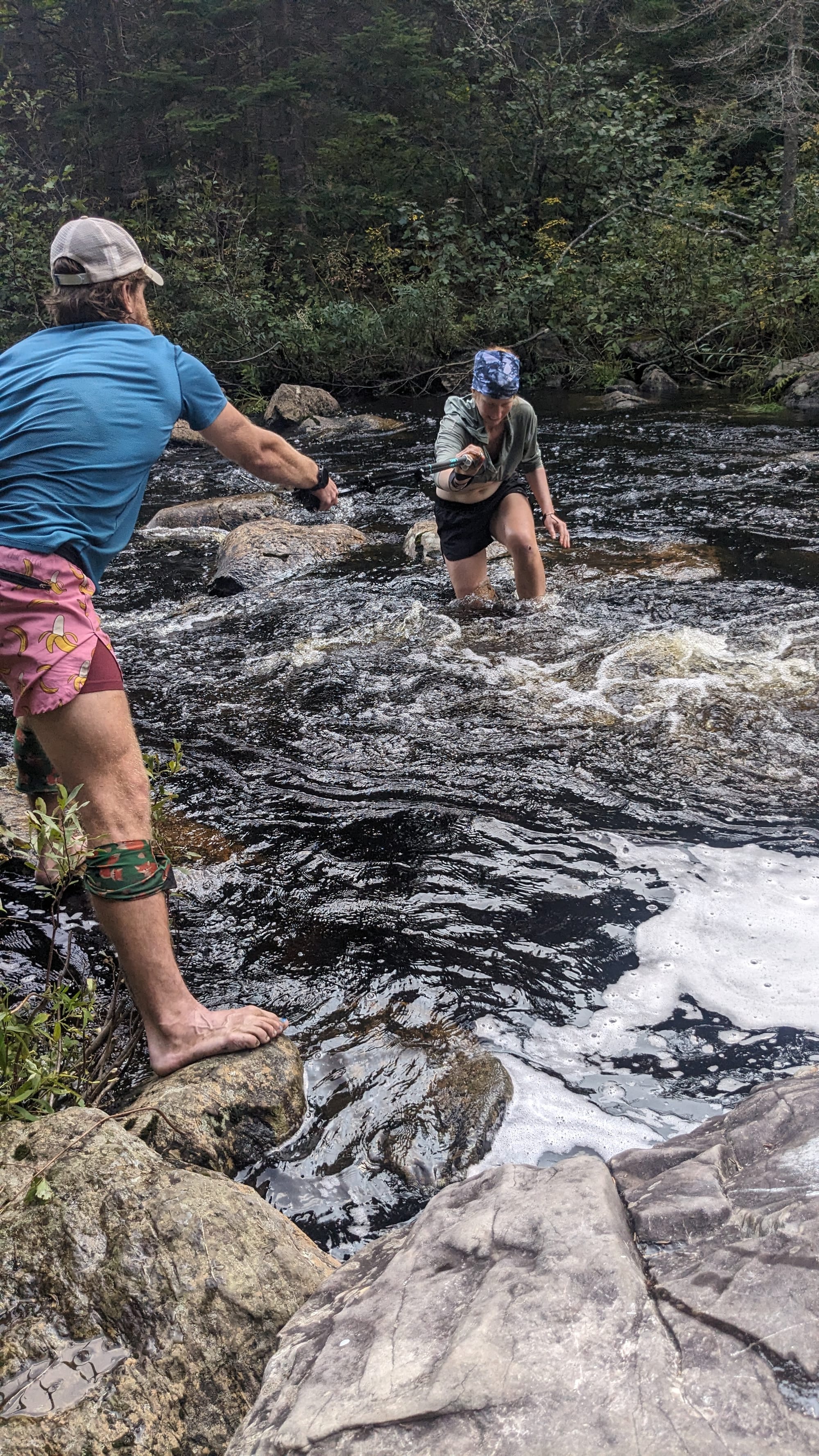 Backpacker stepping across wet rocks in a fast-moving stream on the Appalachian Trail.