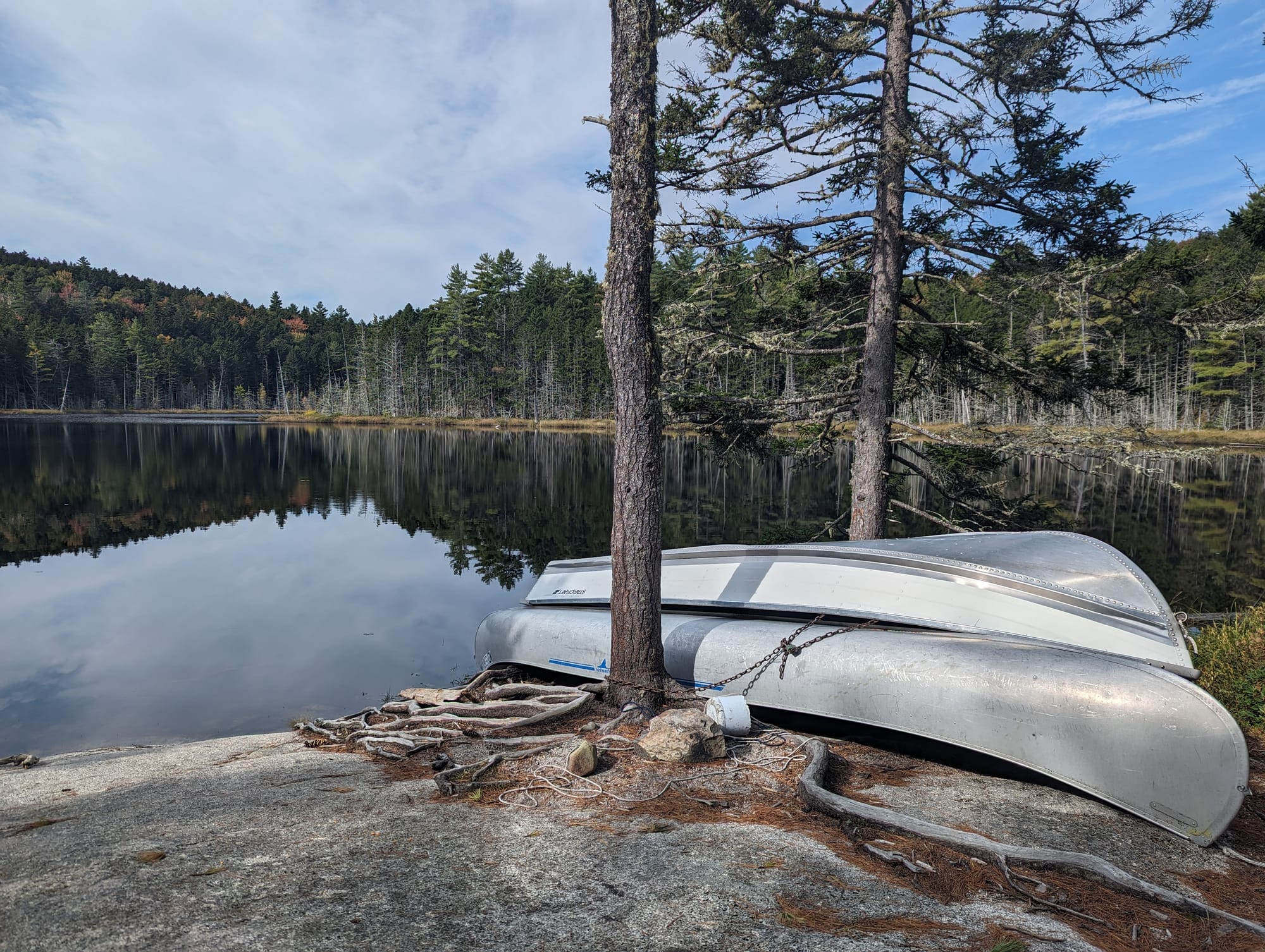 Aluminum canoe resting upside down beside a quiet backcountry lake in Maine.