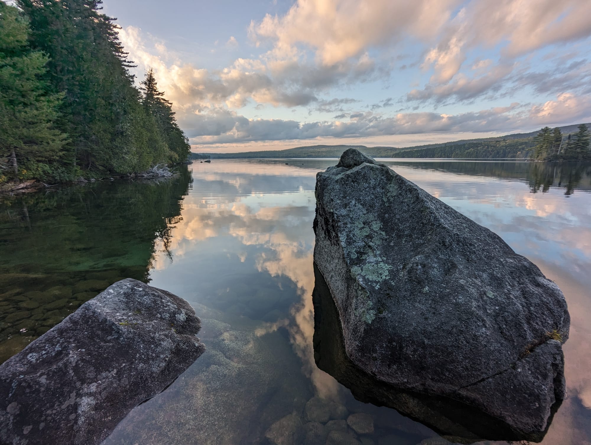 arge boulders along the shore of a calm Maine lake reflecting evening clouds.