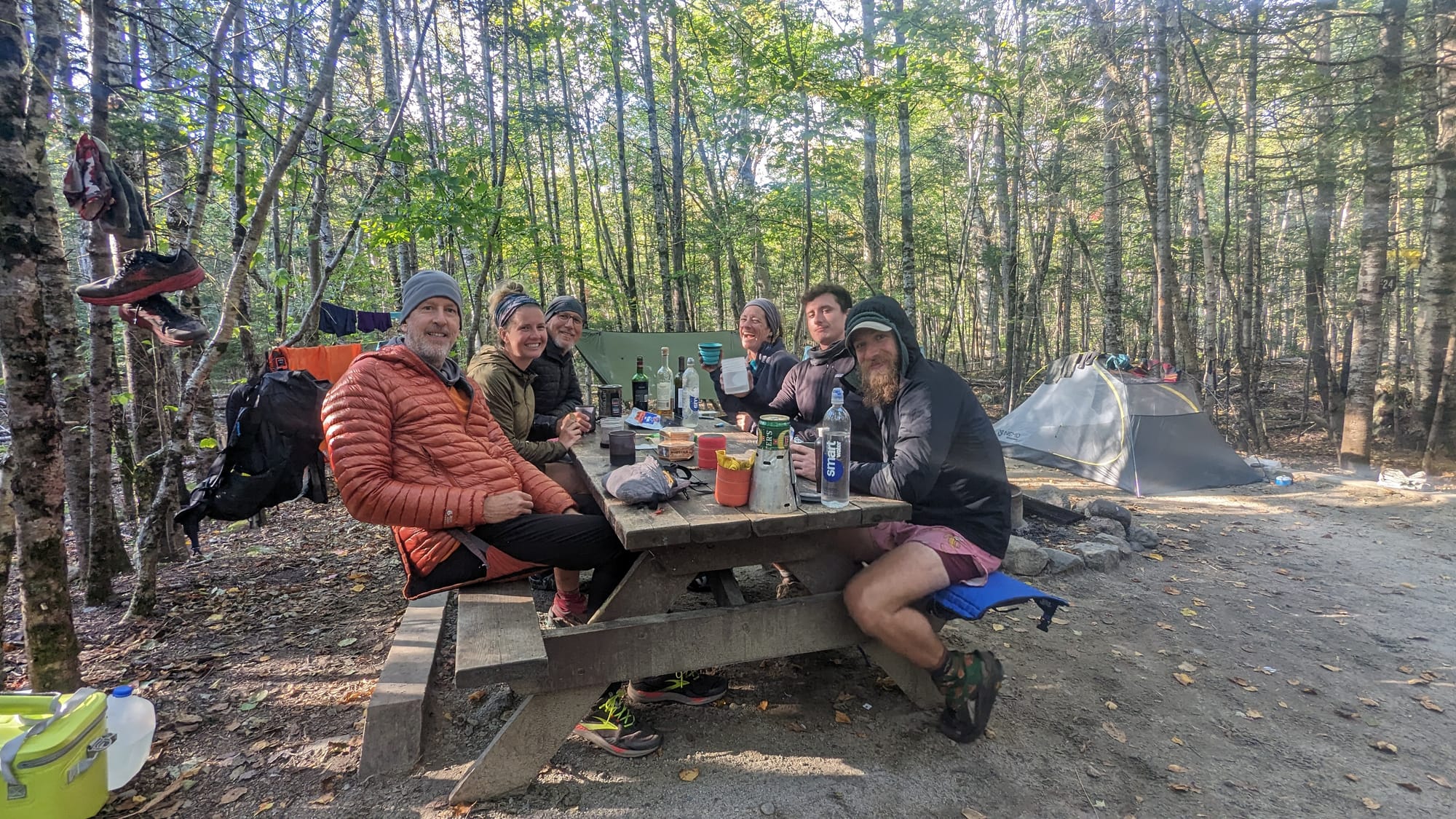 Appalachian Trail hikers gathered around a picnic table at a wooded campsite in Maine.