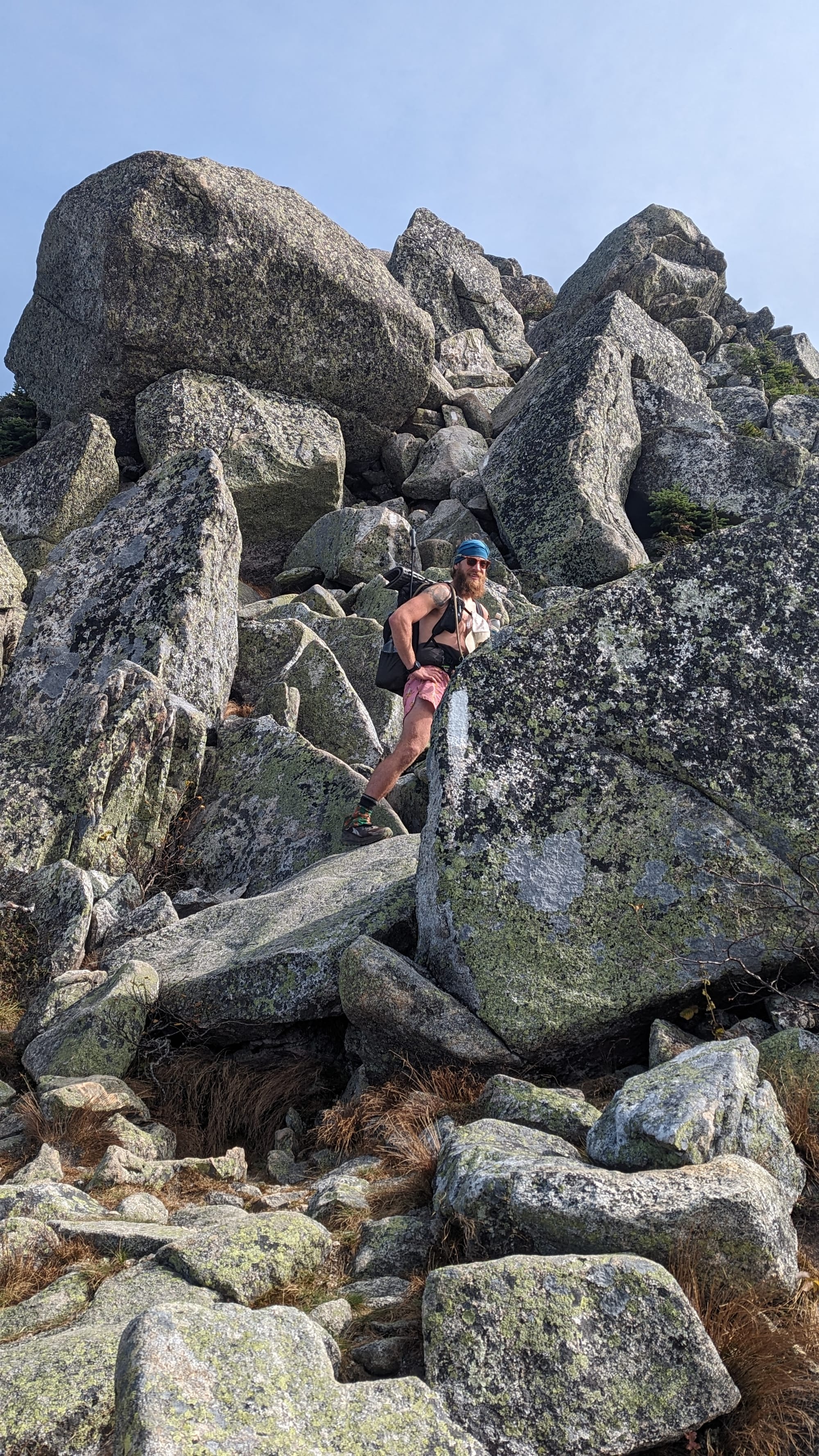Backpacker descending through enormous granite boulders on a steep Appalachian Trail scramble in Maine.