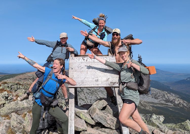 Appalachian Trail thru-hikers celebrating around the Katahdin summit sign at the end of their northbound thru-hike.