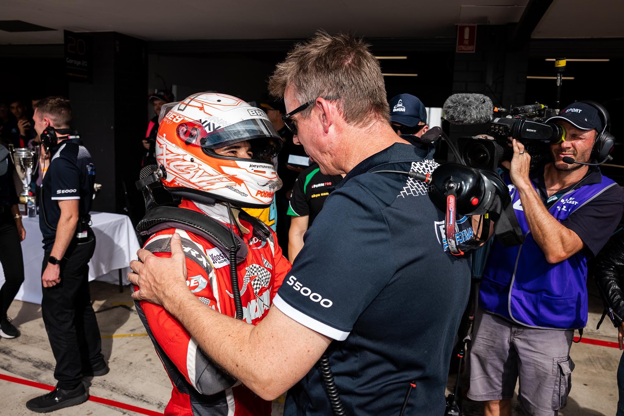 Joey Mawson, wearing a race suit and helmet, celebrates with his team after winning the 2021 S5000 series