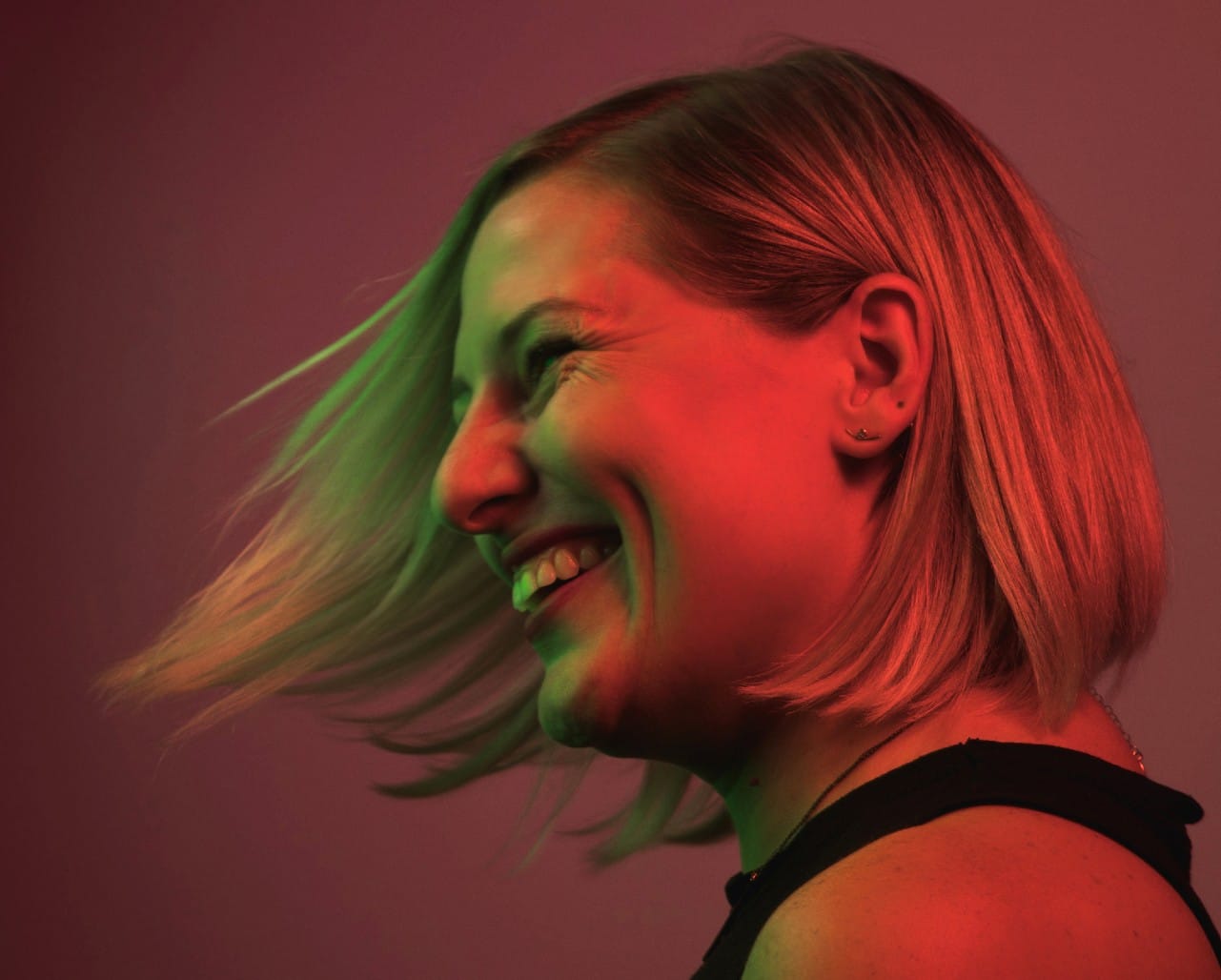 A blonde woman with a bob tossing her hair and grinning widely.