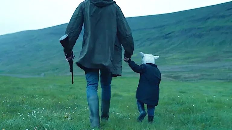 A hybrid lamb-child walks while holding hands with a man with a rifle.